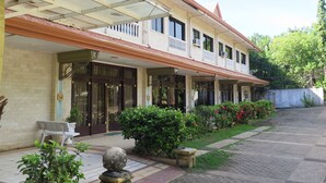 A two-story building with a covered entrance, a balcony on the upper floor, and a garden area with plants and a bench. - Bohol Divers Resort (Tagbilaran)