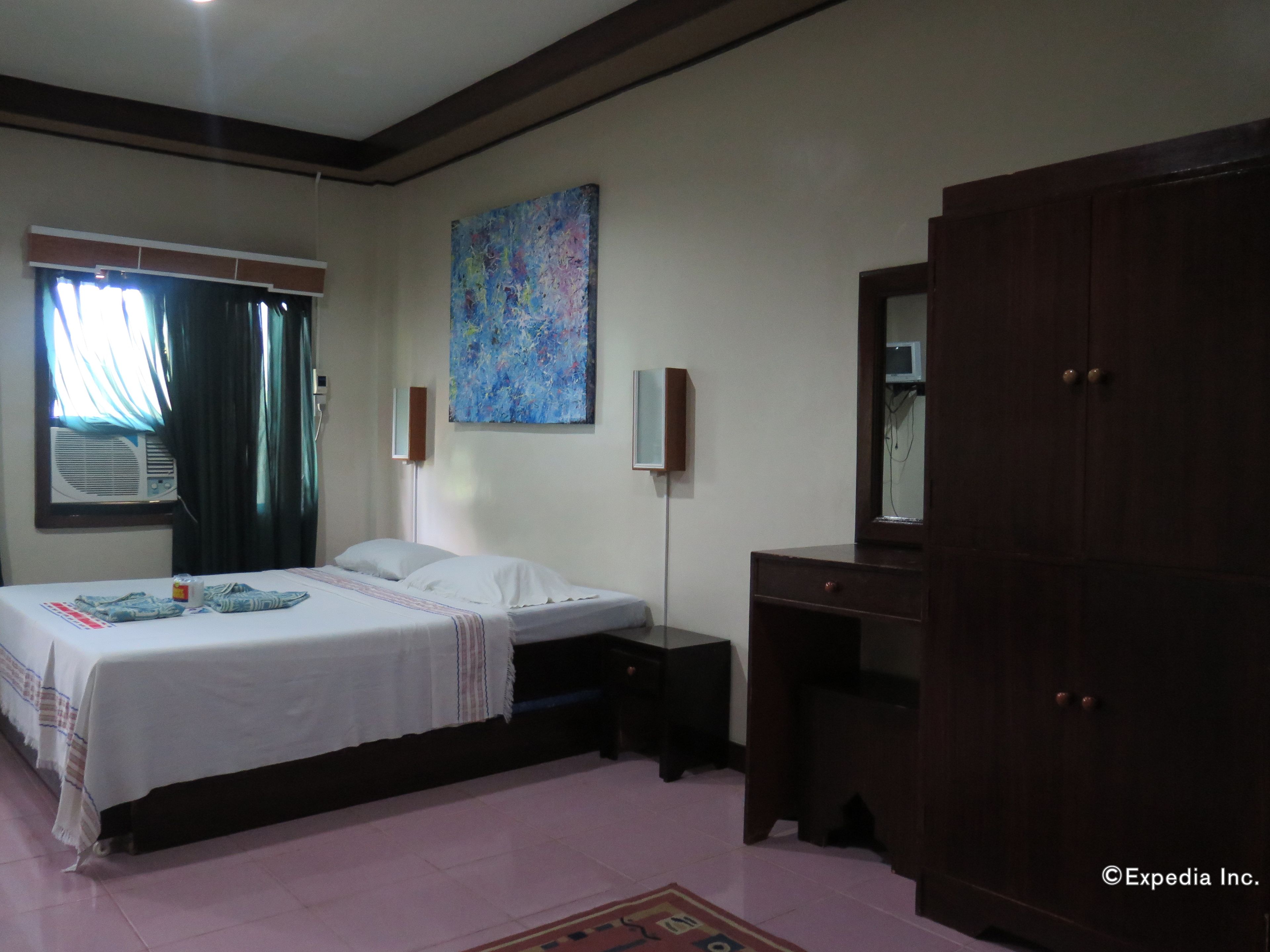 A bedroom with a bed, bedside table, dresser, and a painting on the wall.