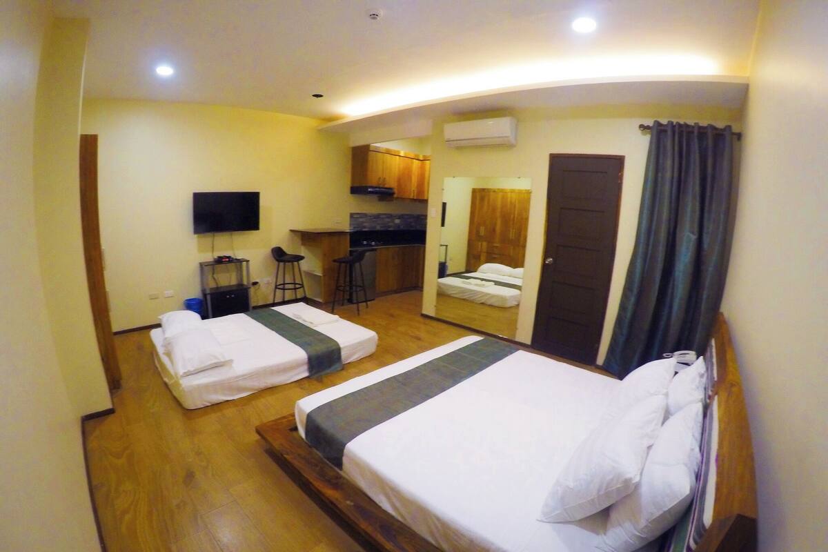 Una habitación de hotel con dos camas, televisión, kitchenette y espejo.