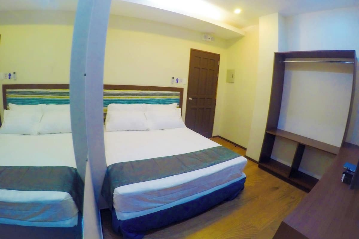 Habitación de hotel con dos camas, piso de madera, una puerta y un estante pequeño.
