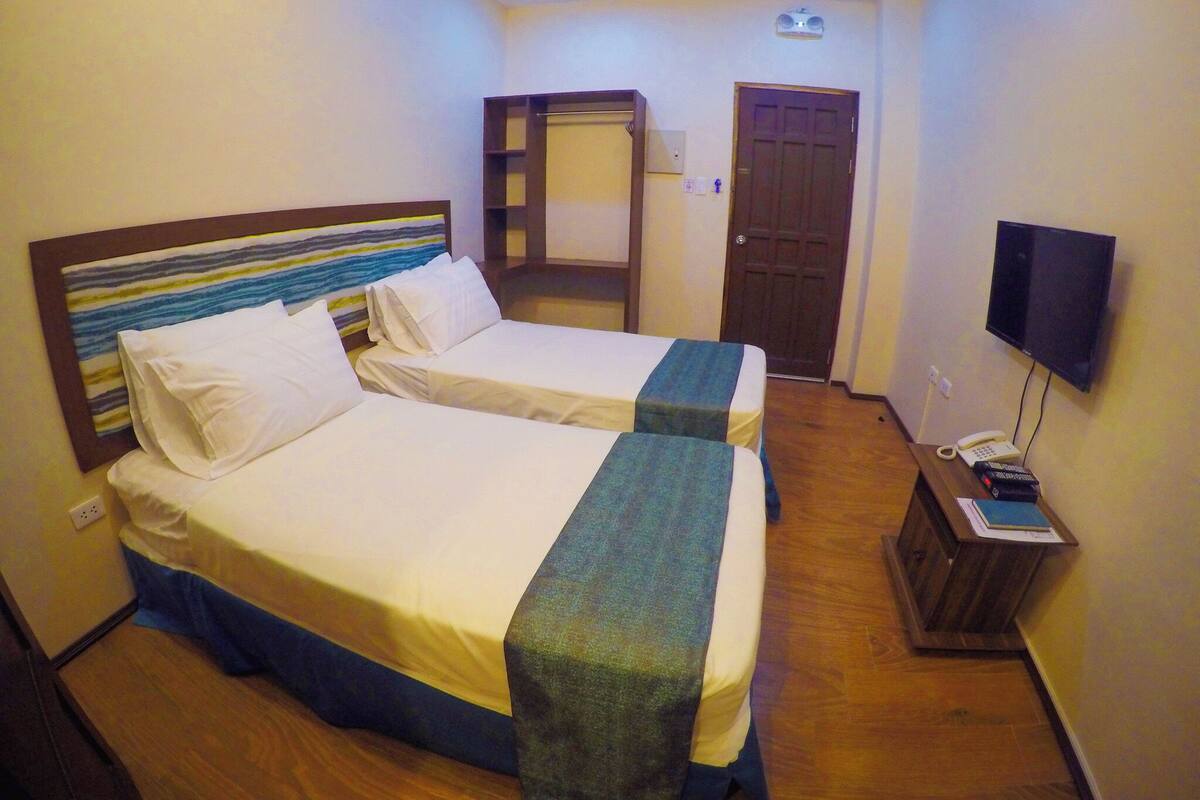 Habitación de hotel con dos camas, un armario, un televisor y un teléfono sobre una mesita de madera.