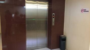 An elevator with a no-smoking sign, a trash bin, and a digital display.