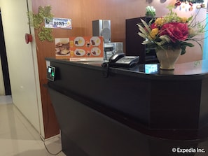 A hotel reception desk with a phone, a menu board, and a flower vase.
