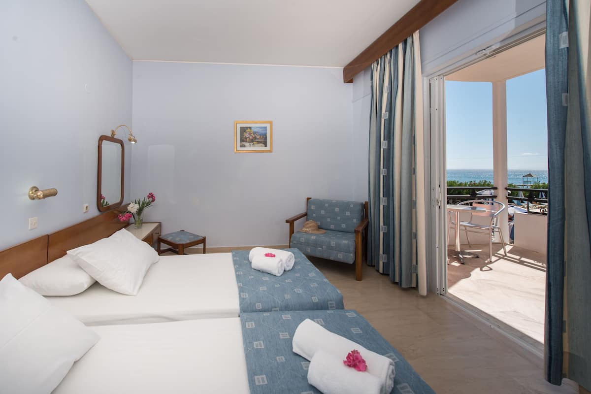 A hotel room with two beds, a chair, a small table, a mirror, and a view of the sea.