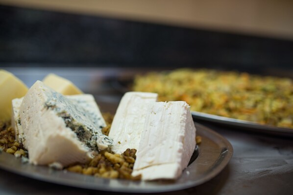 A plate of cheese with a variety of textures and a tray of mixed vegetables in the background.