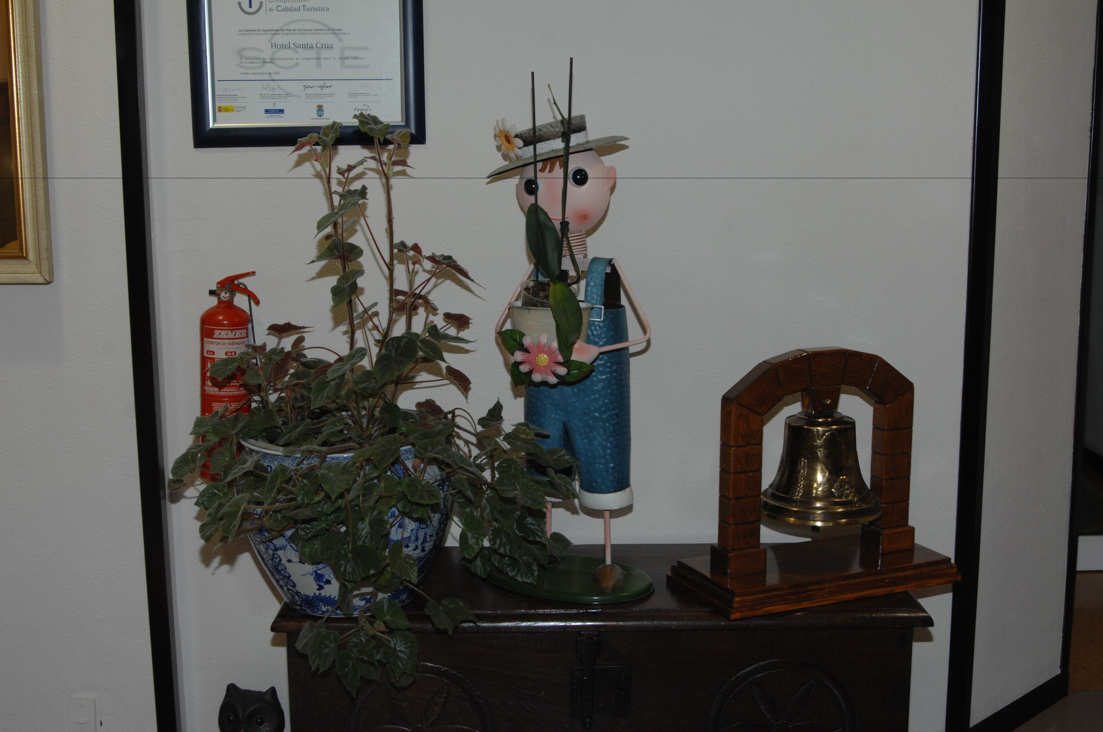 A decorative display with a potted plant, a figurine, and a bell on a wooden stand.
