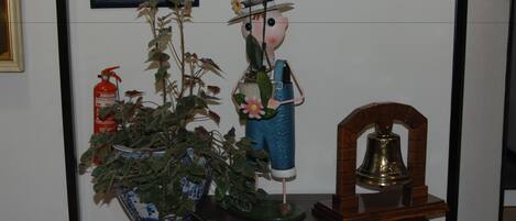 A decorative display with a potted plant, a figurine, and a bell on a wooden stand.