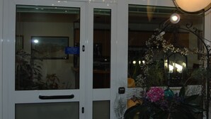 Ein Hotel Eingang mit Glastür, einem Schild darüber und einer dekorativen Pflanzengestaltung außen.