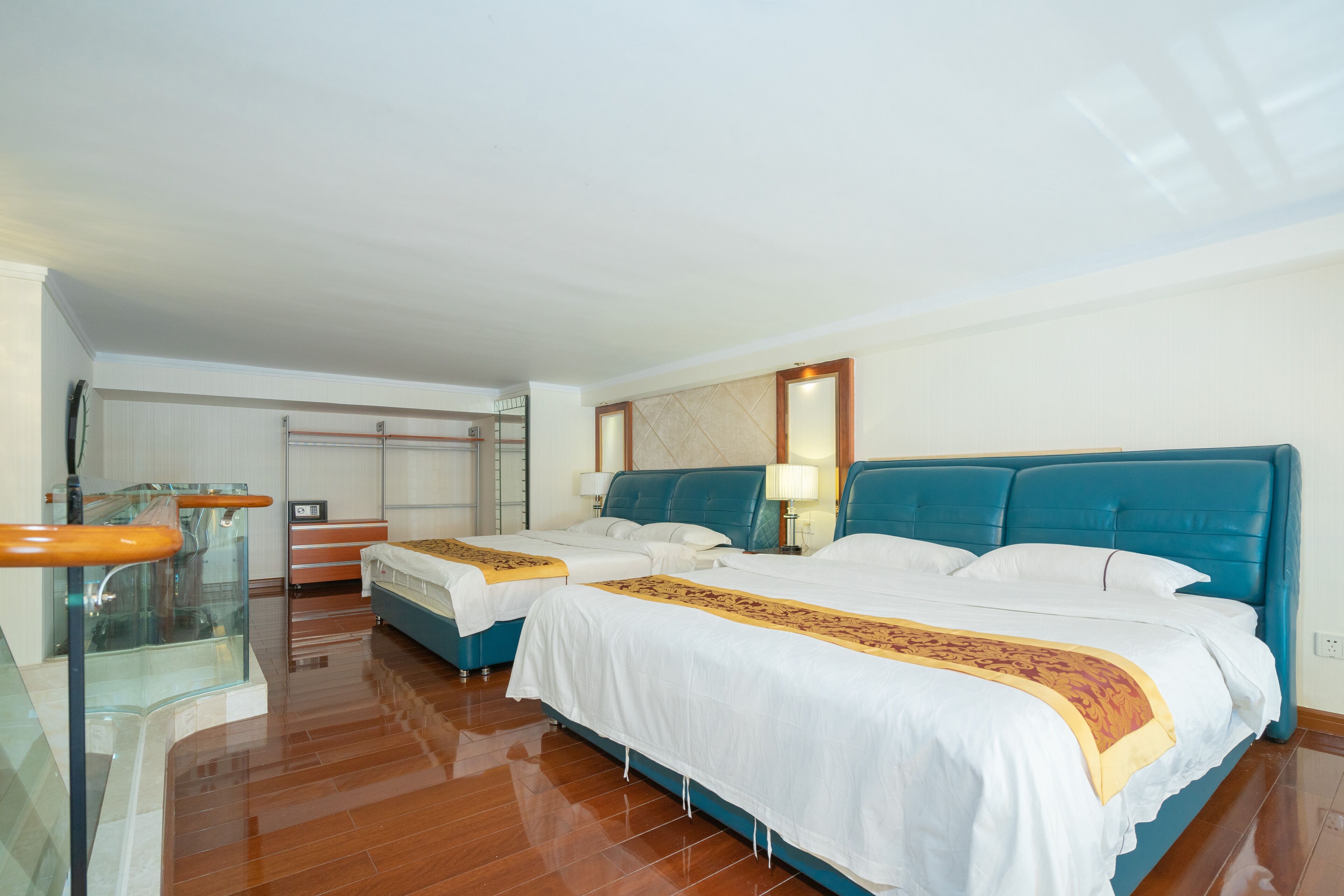 Habitación de hotel con dos camas, barandilla de vidrio y piso de madera.