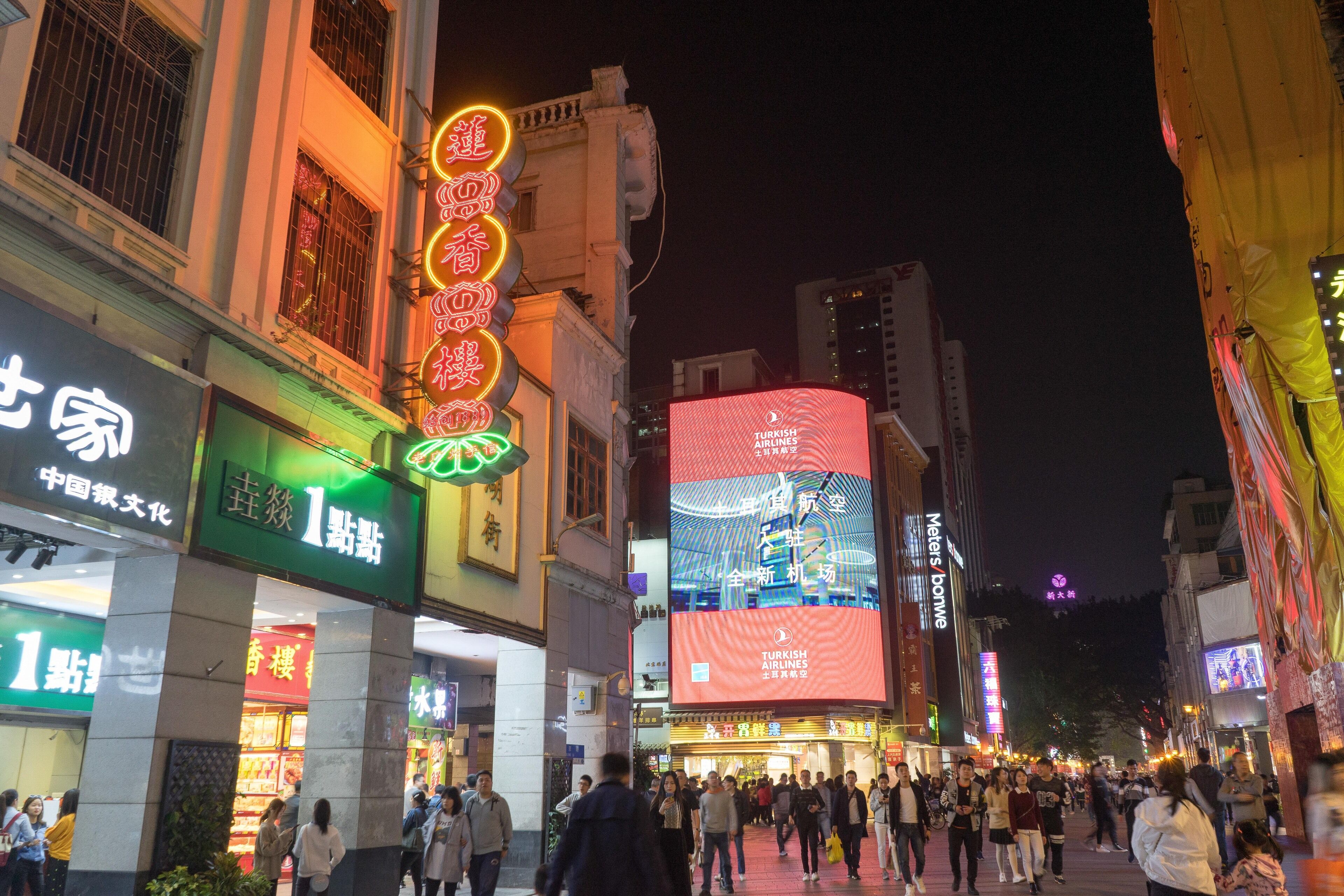 A busy urban street at night with illuminated signs and billboards, including a prominent Turkish Airlines advertisement.