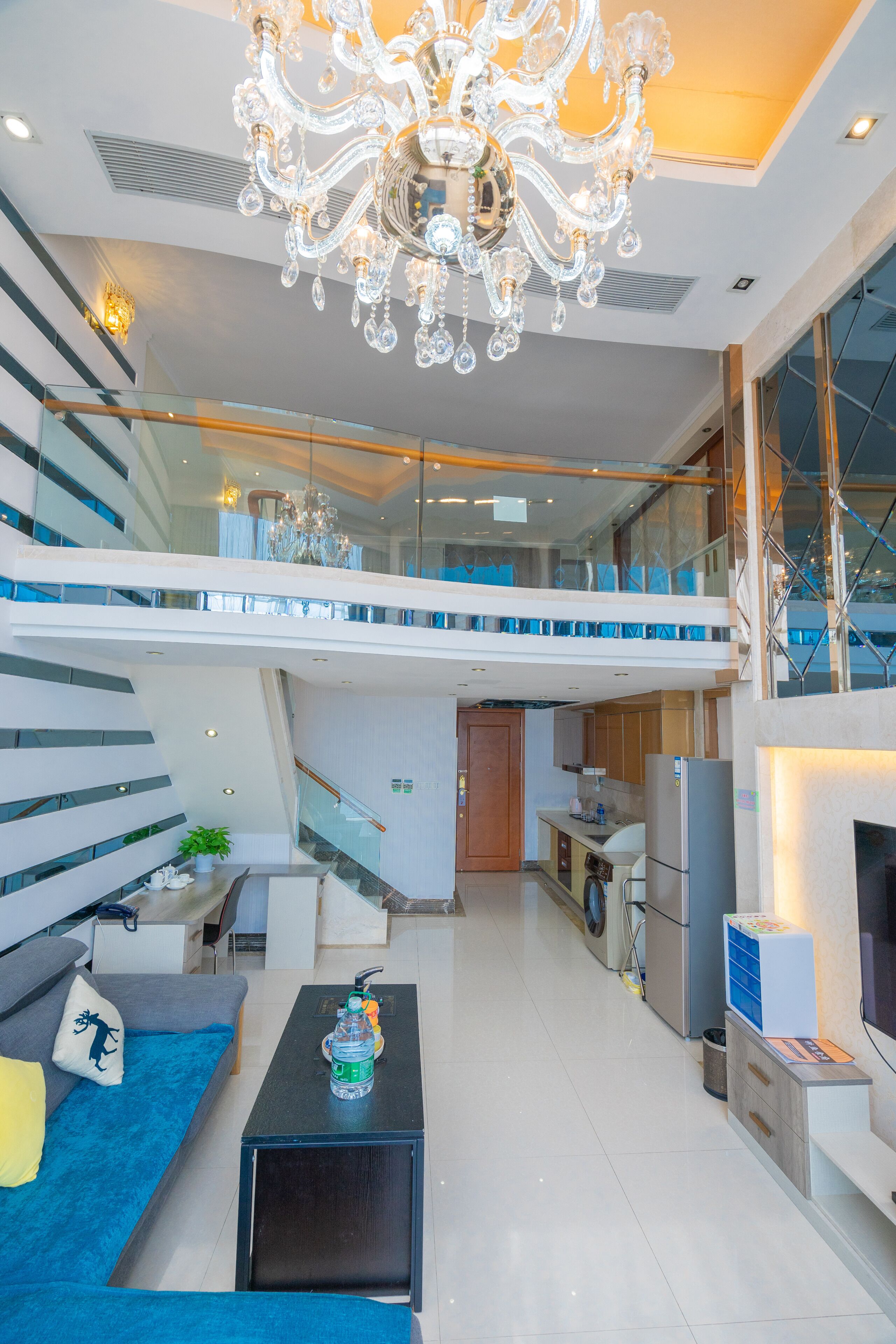 A modern apartment with a staircase leading to a balcony, a kitchen area, and a living room with a sofa and coffee table.