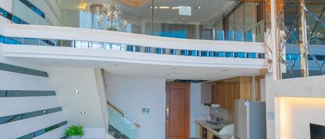 A modern apartment with a staircase leading to a balcony, a kitchen area, and a living room with a sofa and coffee table.