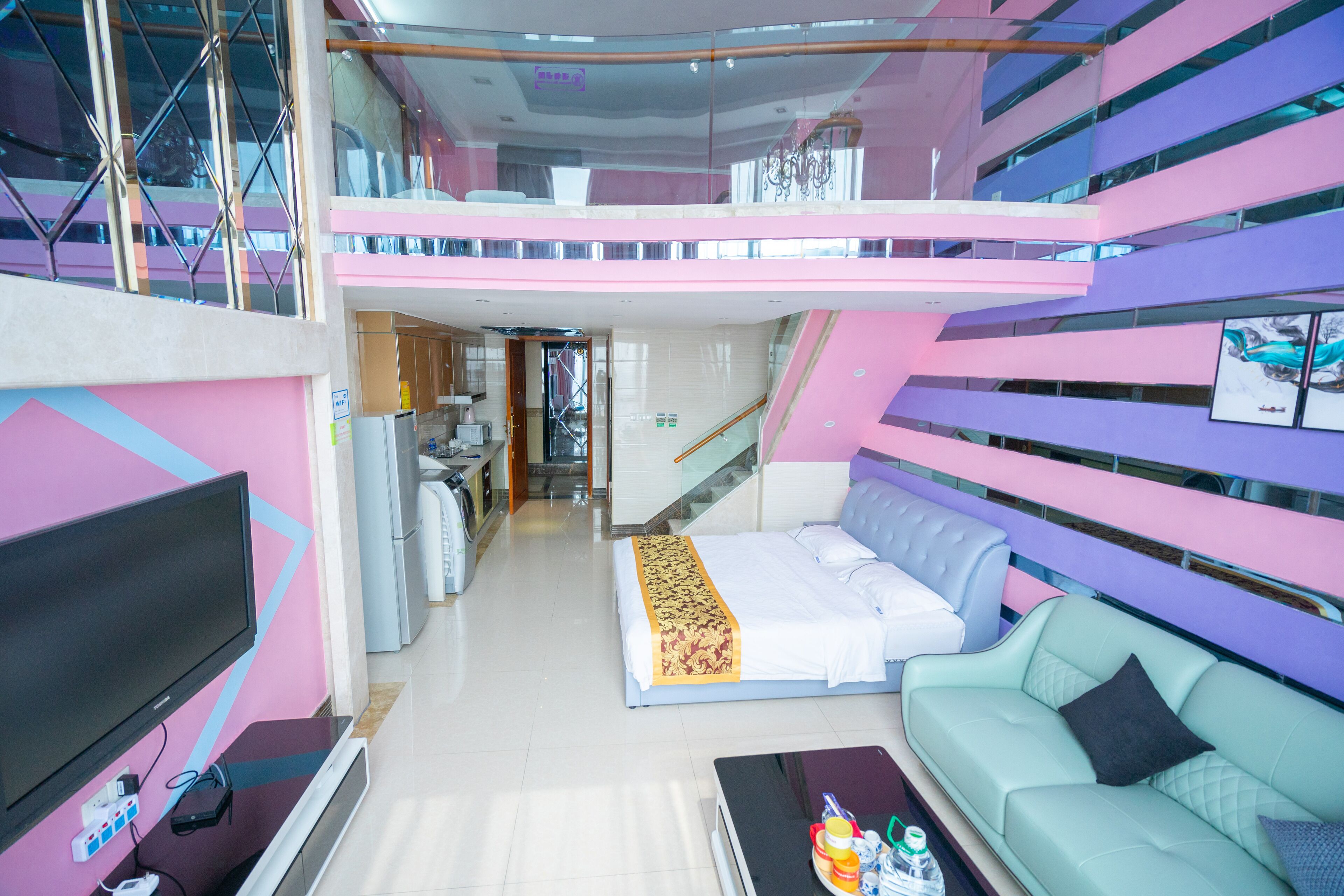 A modern hotel room with a bed, a sofa, a TV, and a kitchenette.