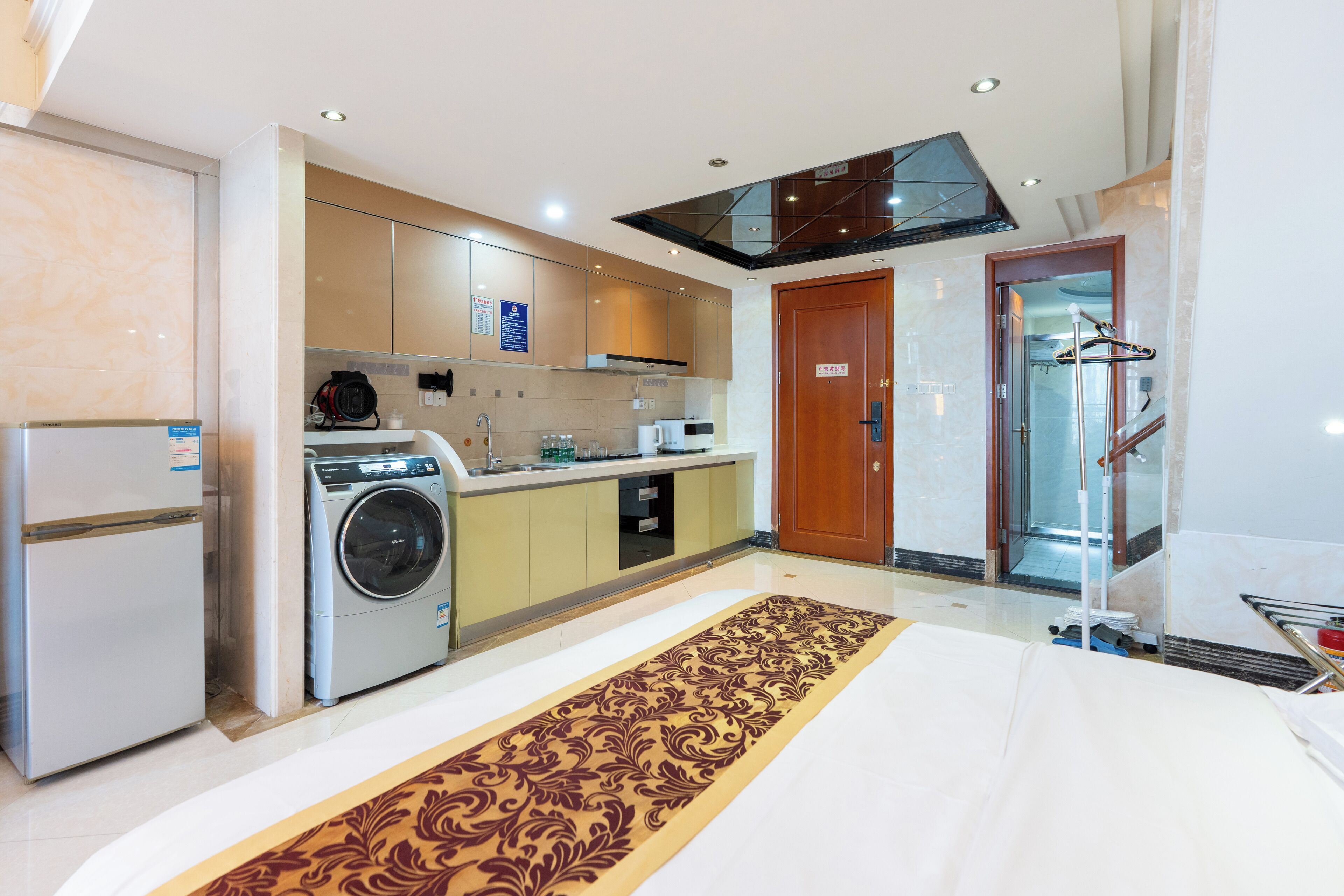 Una habitación de hotel moderna con zona de cocina, que incluye un refrigerador, lavadora y comedor con mesa y sillas.
