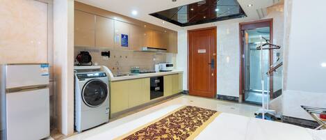 Una habitación de hotel moderna con zona de cocina, que incluye un refrigerador, lavadora y comedor con mesa y sillas.