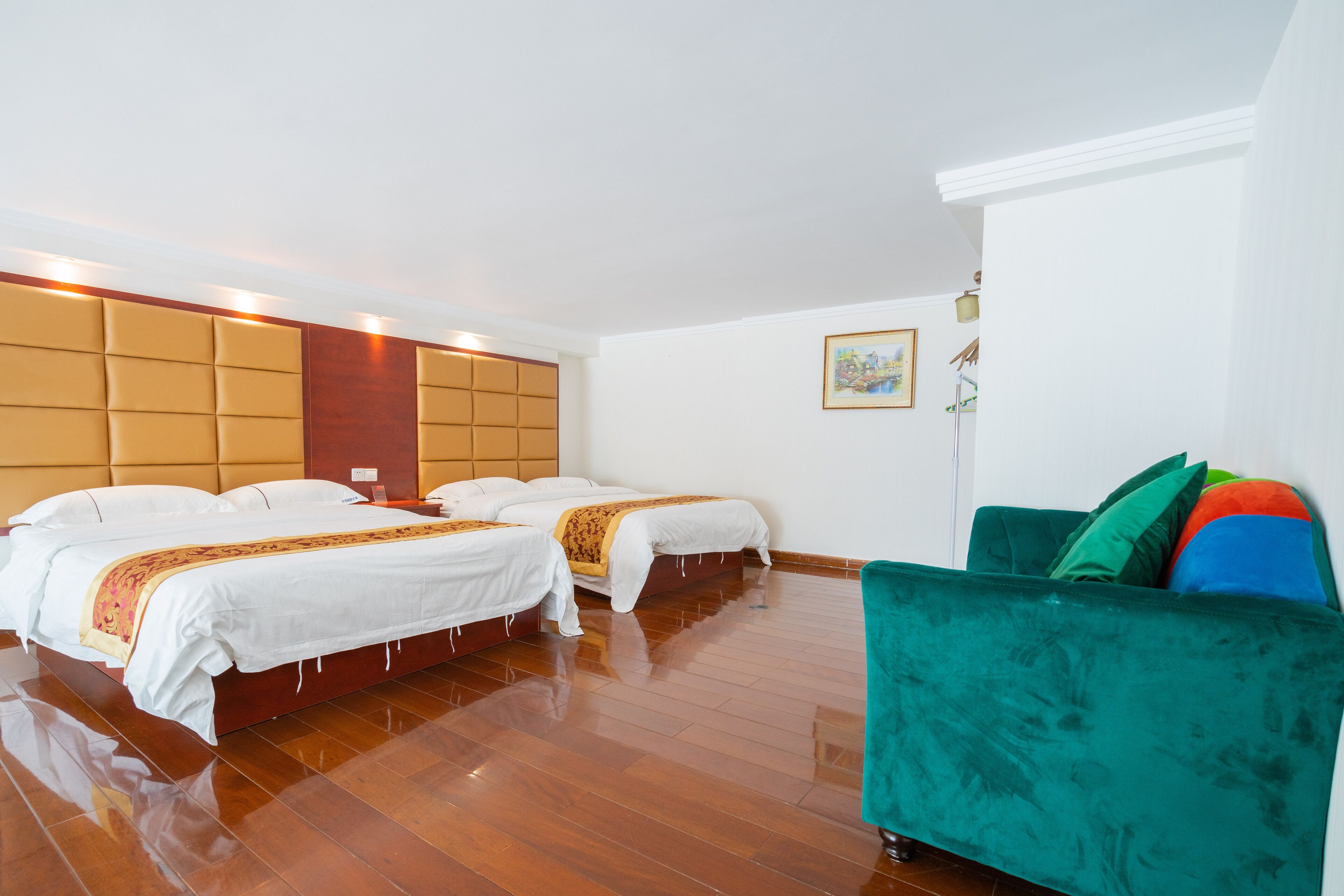 A hotel room with two beds, a green sofa, wooden flooring, and a painting on the wall.