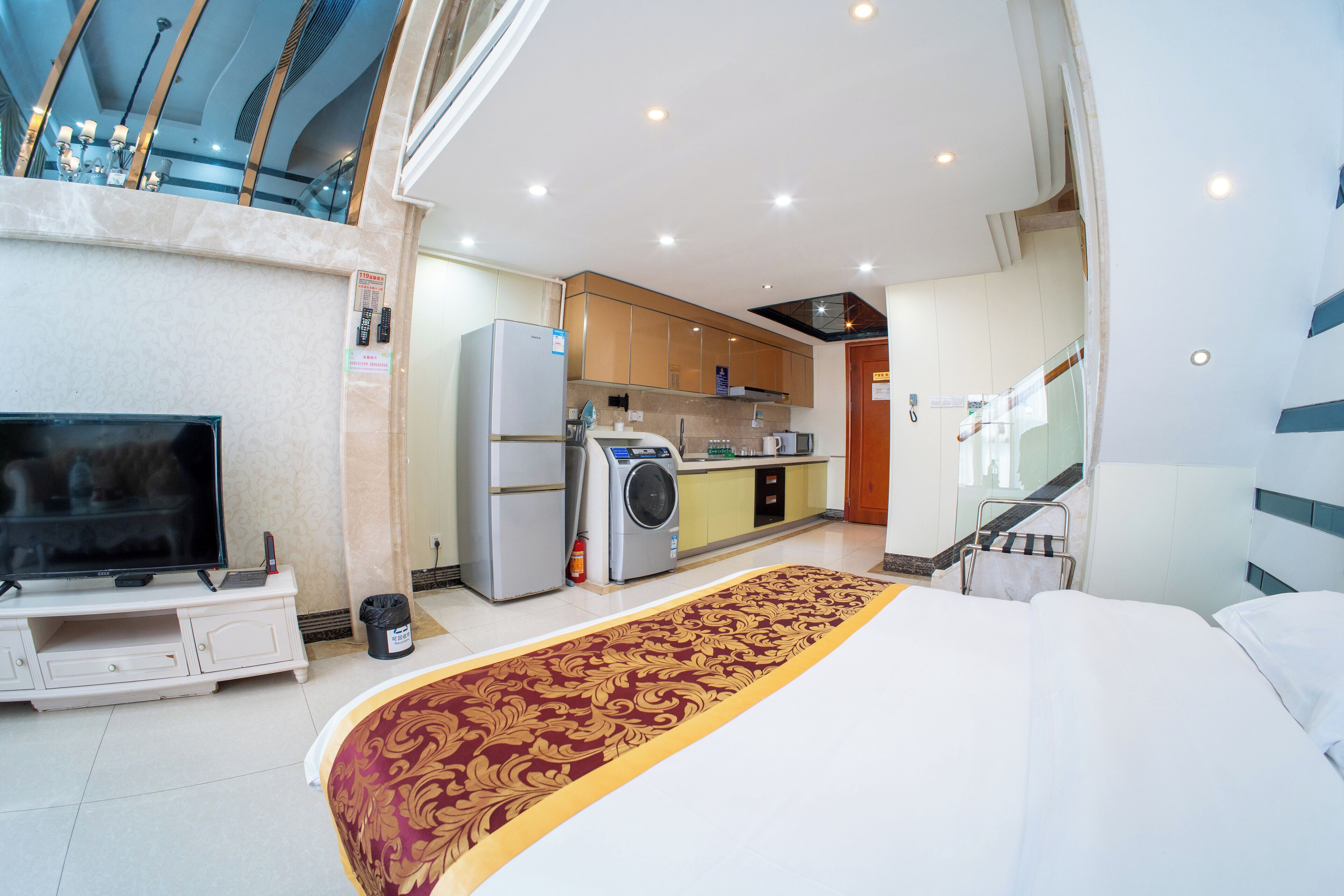 A hotel room with a large bed, a television, a washing machine, and a kitchenette.