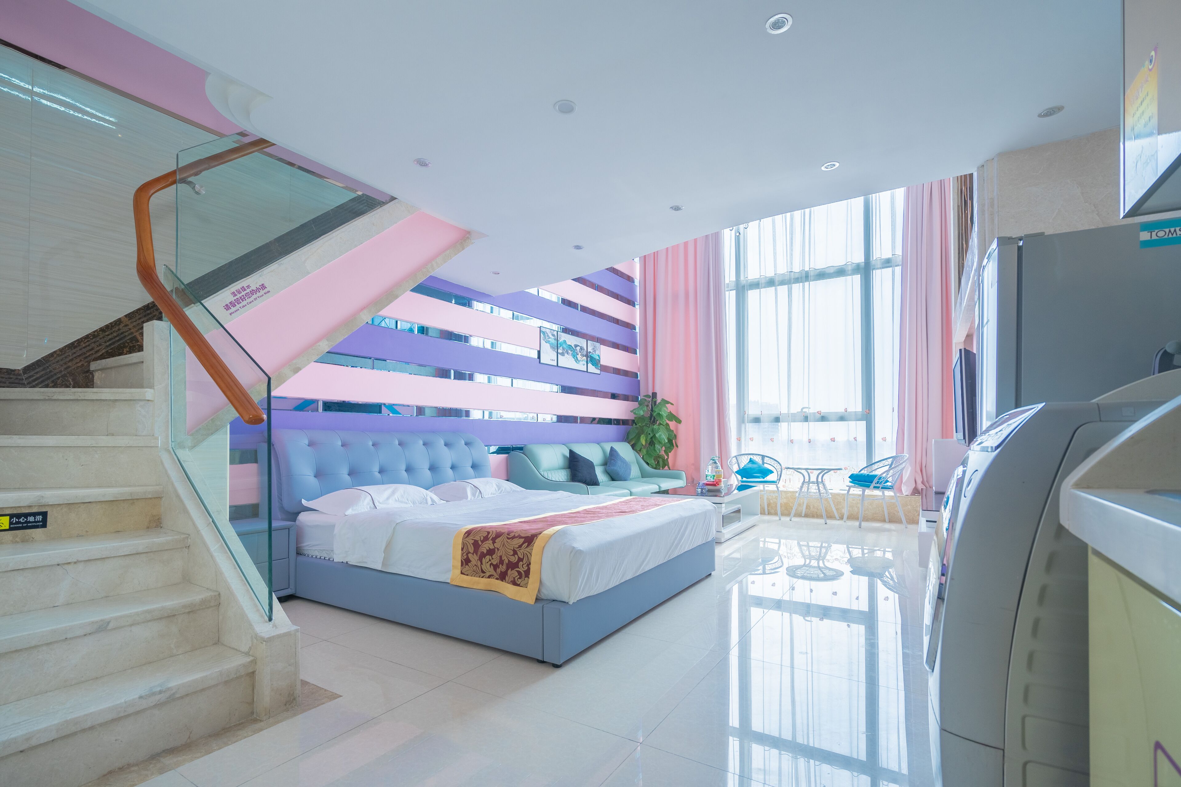 A modern hotel room with a bed, a staircase, a seating area, and a large window.