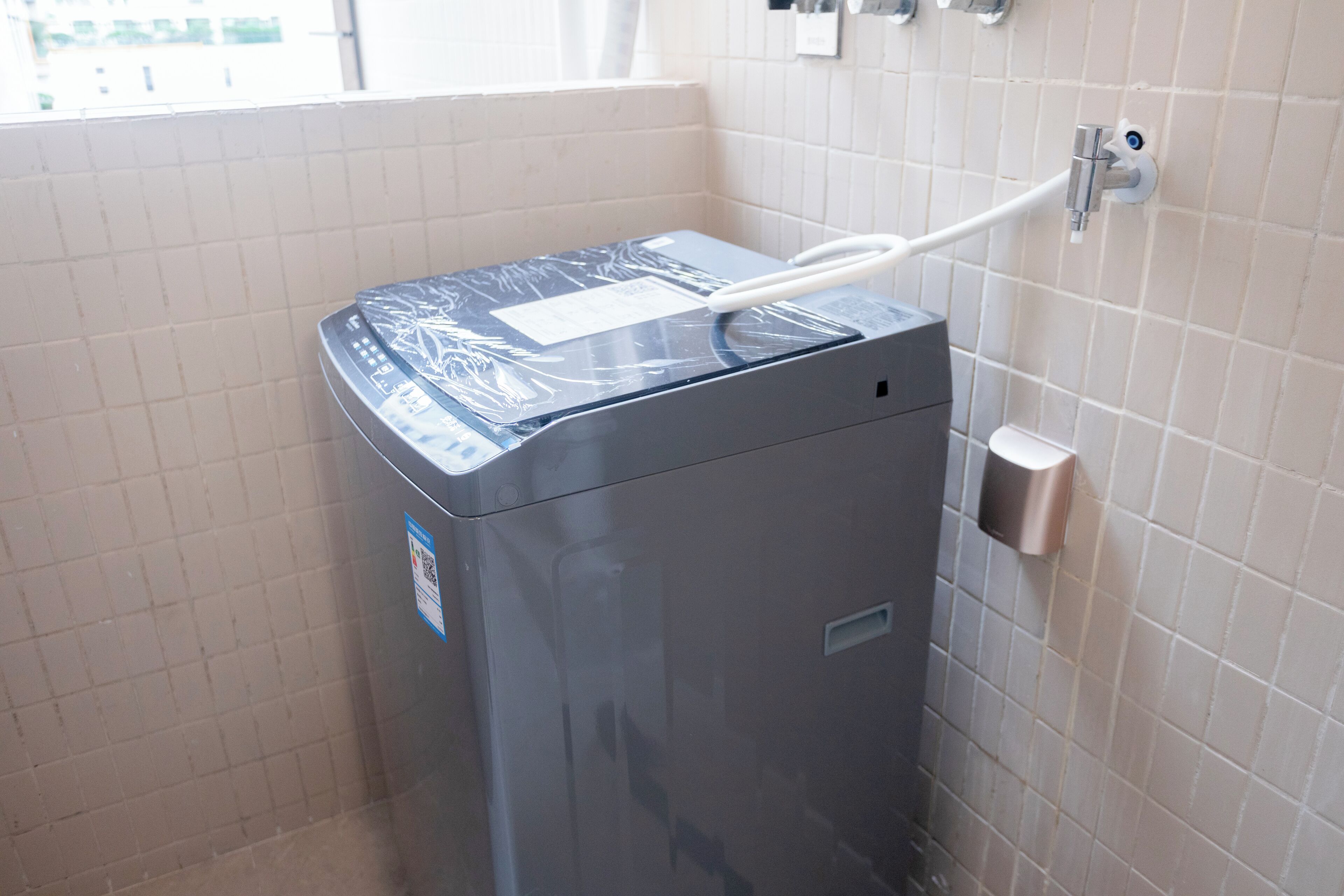 Een compacte, moderne wasmachine in een kleine betegelde badkamer met een raam.