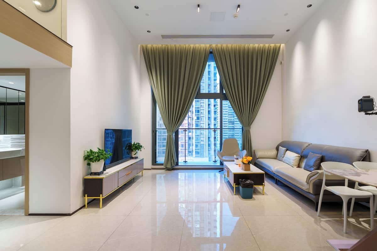 A modern living room with a sofa, TV, and a large window with curtains.