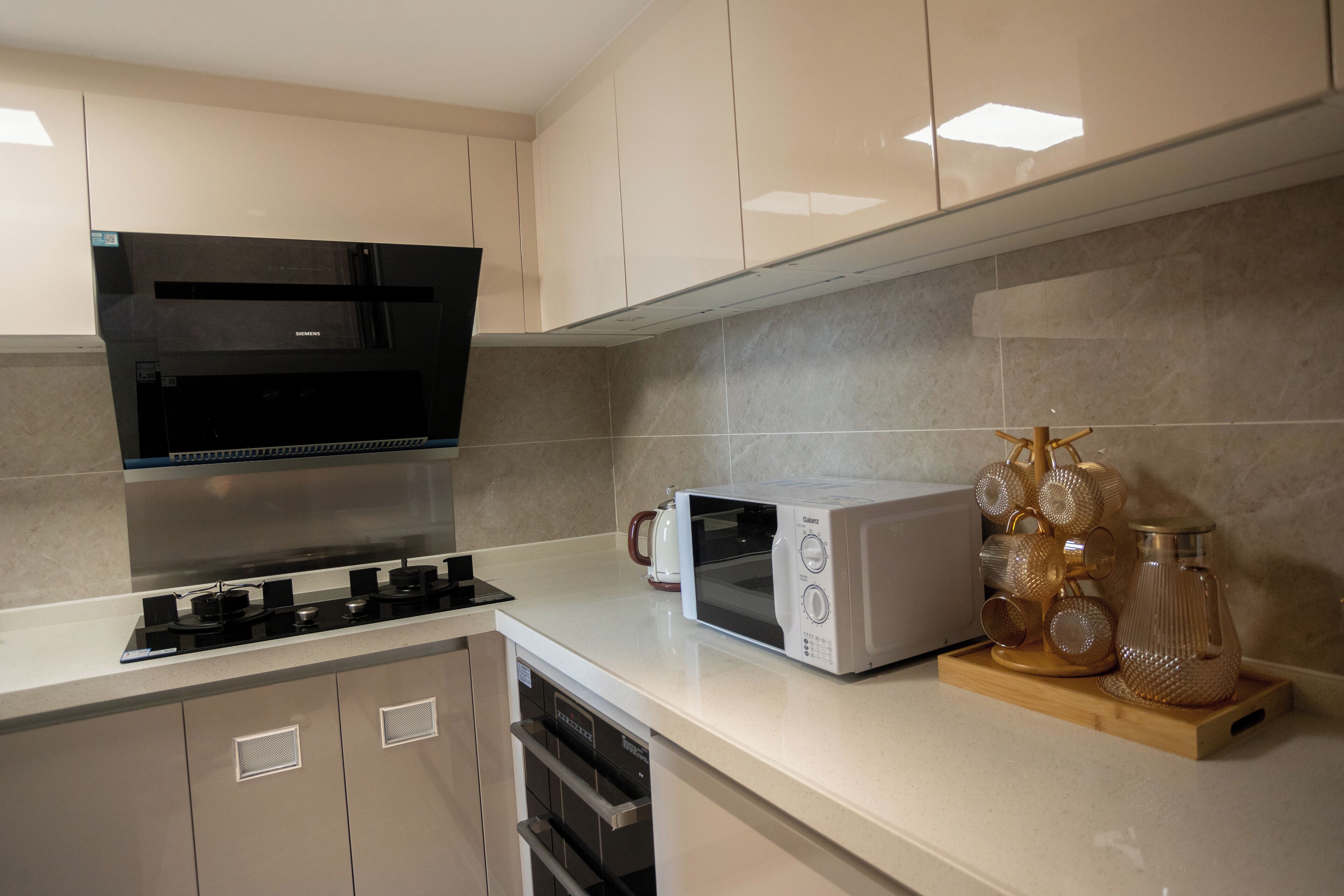 Une cuisine moderne équipée d’une cuisinière, d’un four à micro-ondes et d’un four encastrés, ainsi que d’une machine à café et de beaux verres décoratifs posés sur le plan de travail.