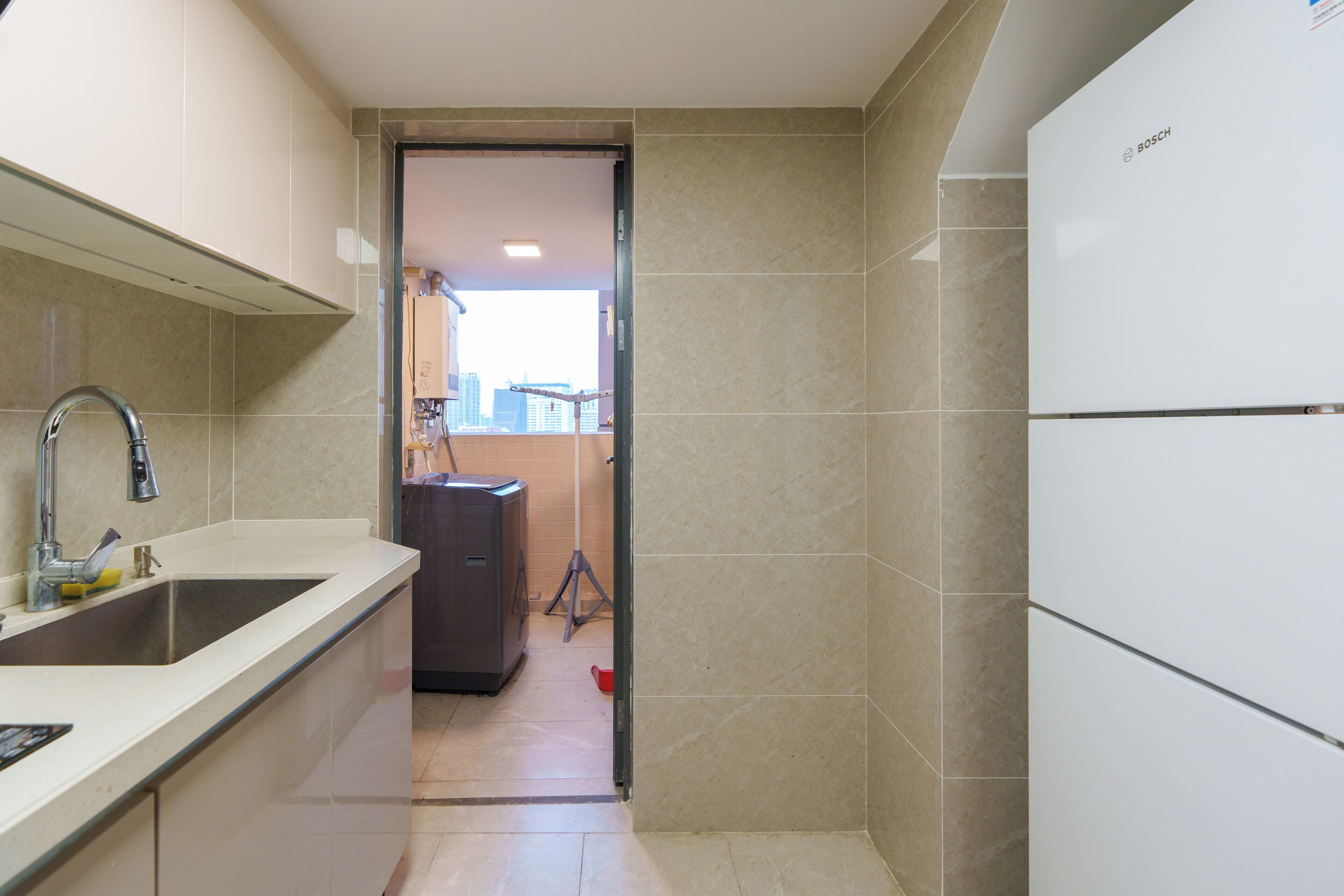 Una cocina moderna con un lavaplatos integrado, un refrigerador Bosch y vista al área de estar mediante una puerta abierta.