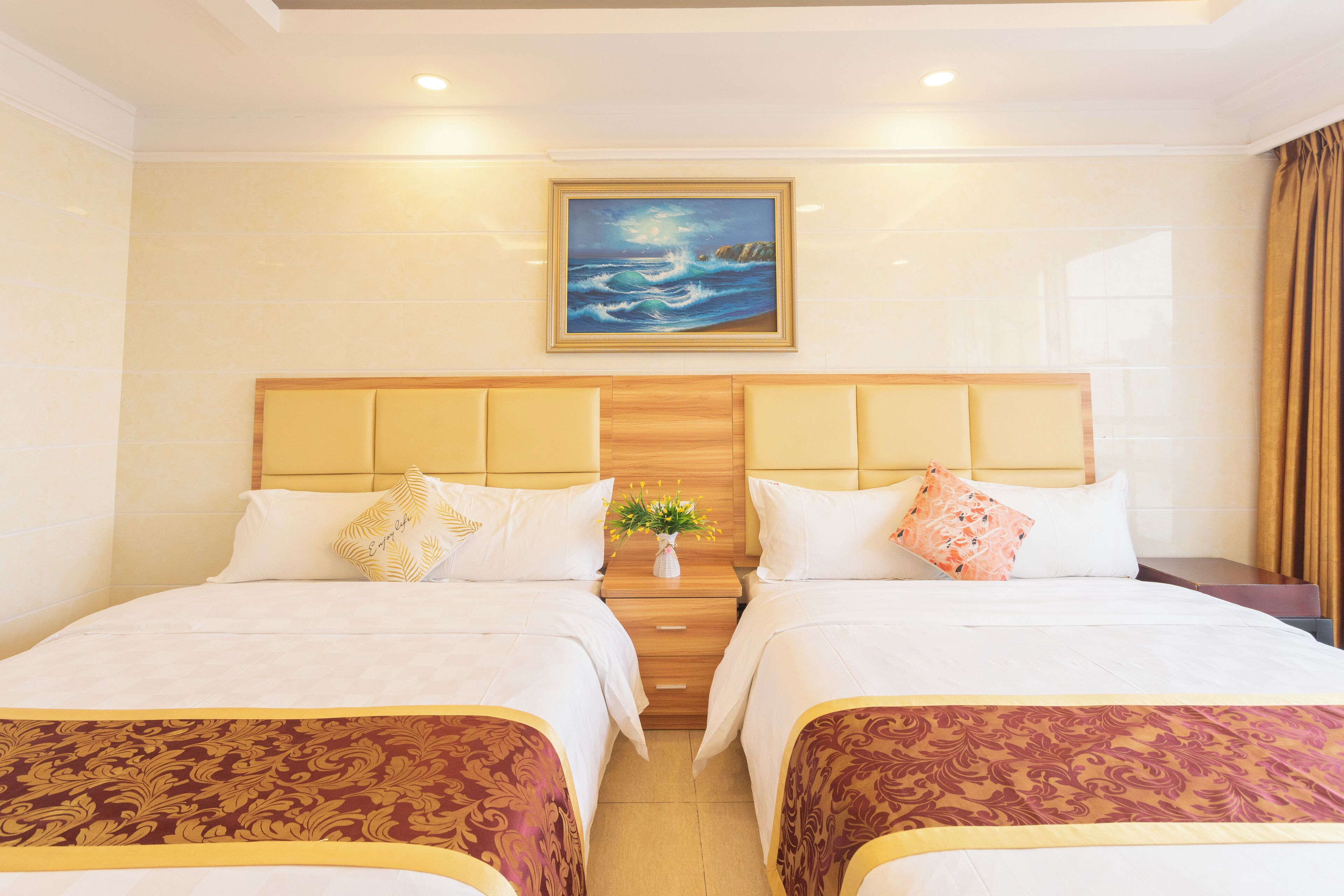 A hotel room with two beds, a nightstand with a vase of flowers, and a painting on the wall.
