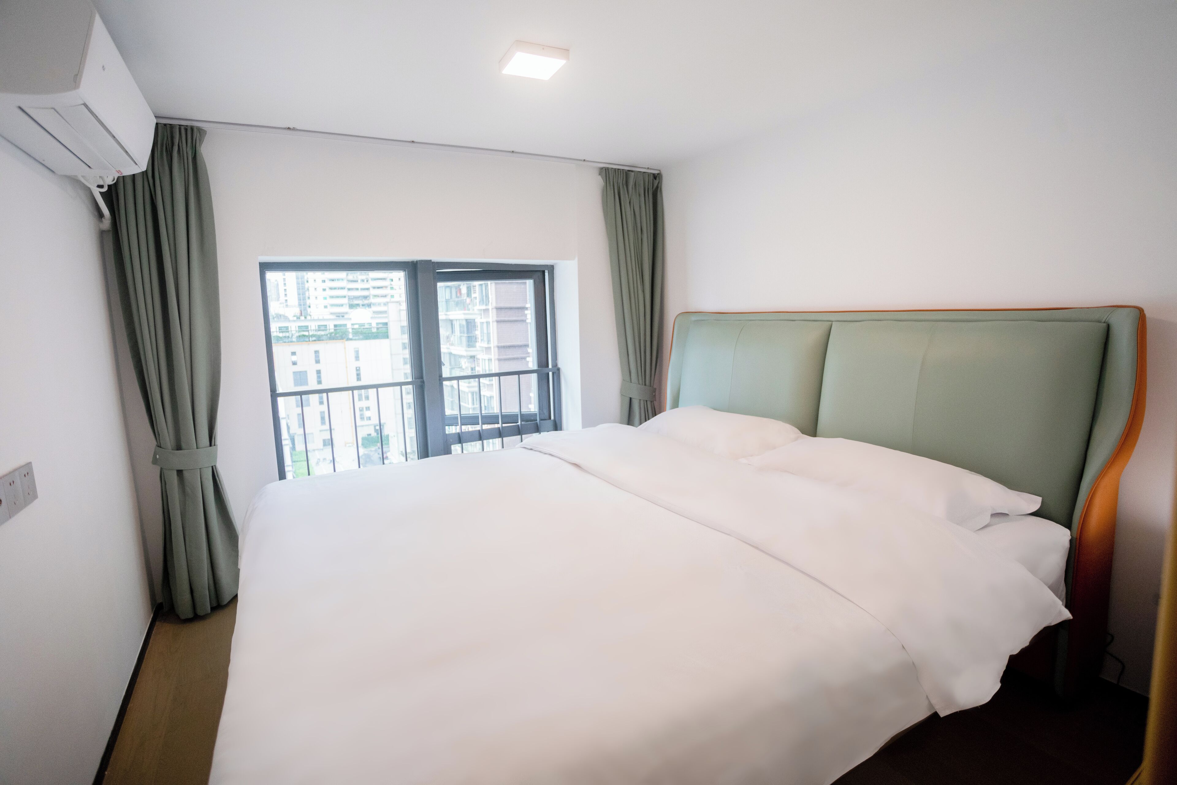 Una habitación de hotel con una cama grande, una ventana con cortinas y un equipo de aire acondicionado.