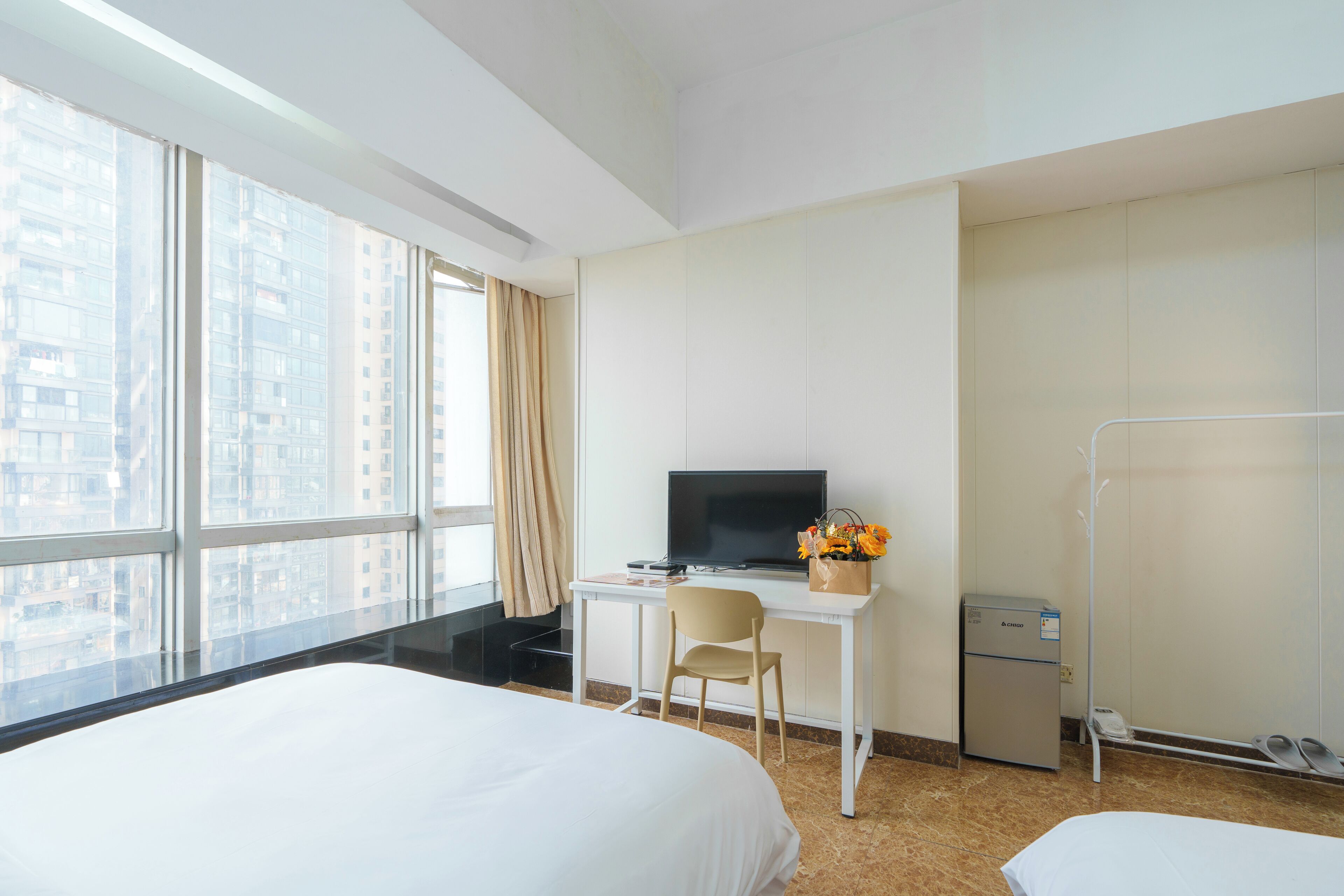 A hotel room with two beds, a desk with a television, a small refrigerator, and a window with a city view.