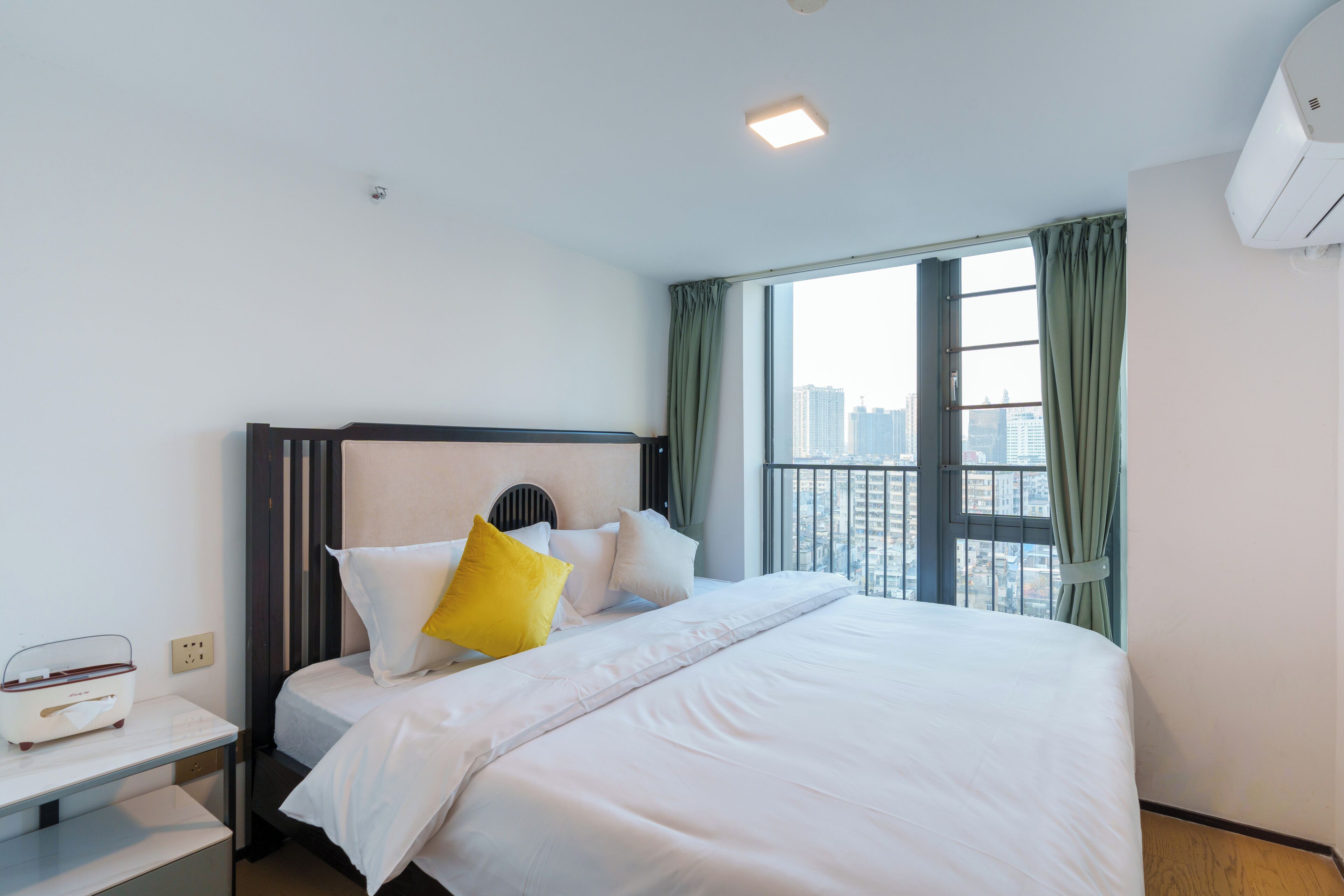 Habitación de hotel con una cama grande, una mesita de noche, una ventana con cortinas y vistas a la ciudad.