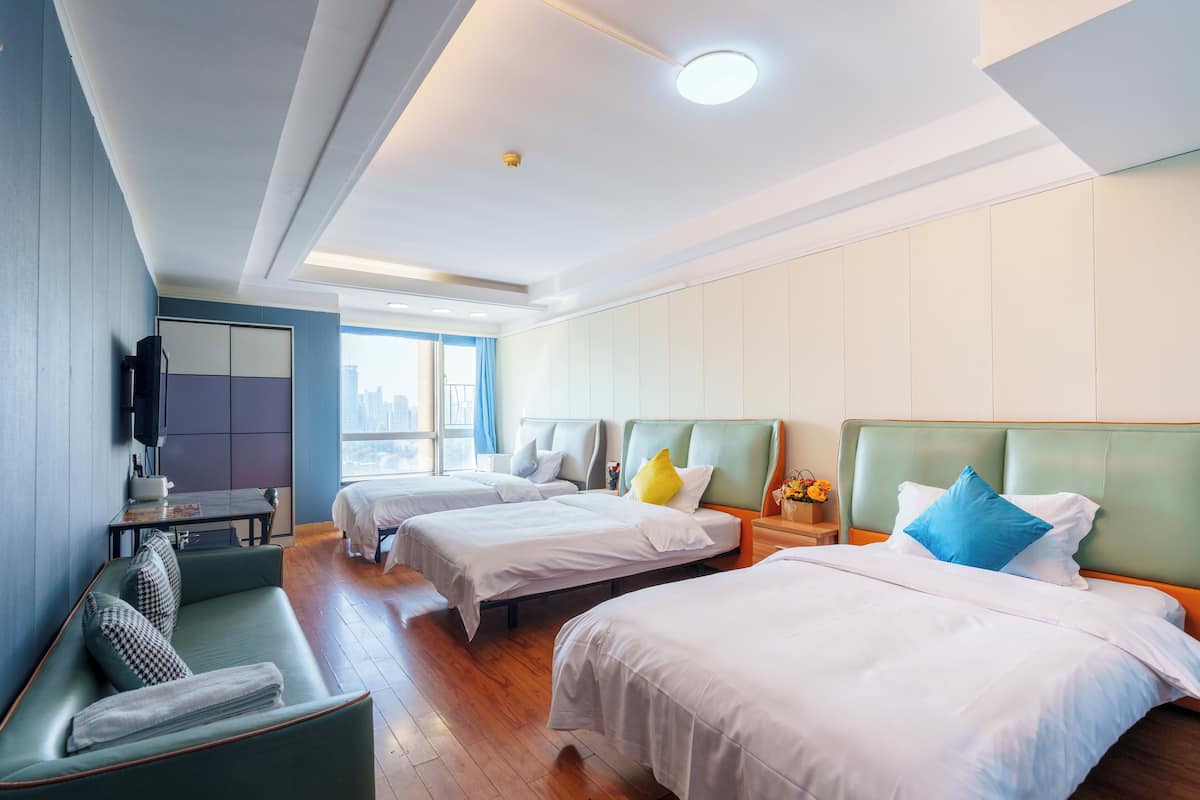 A hotel room with two beds, a sofa, a TV, and a city view.