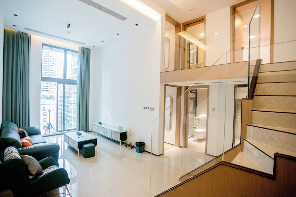 A modern apartment with a living area, a staircase, and a view of the city.