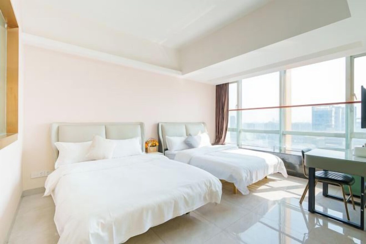 A hotel room with two beds, a desk, and a large window offering a city view.