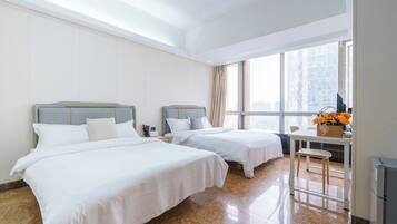 A hotel room with two beds, a desk, and a window with a city view.