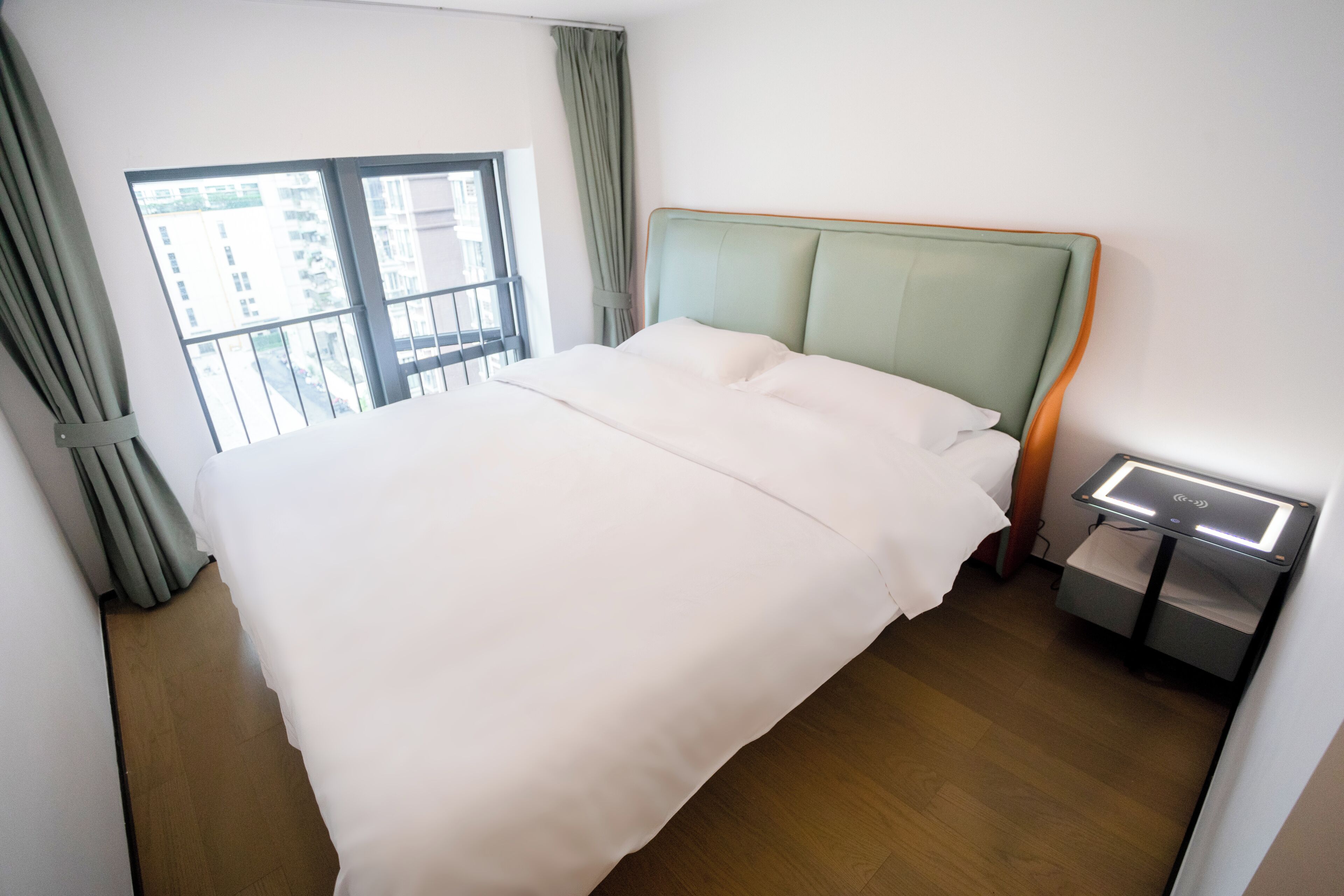 A neatly made bed with a wooden headboard, a bedside table with a lamp, and a window with curtains.