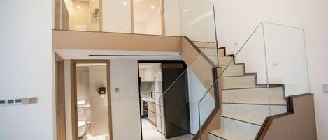 Un interior moderno con una escalera de cristal que lleva a un segundo piso, una zona de cocina y un baño.