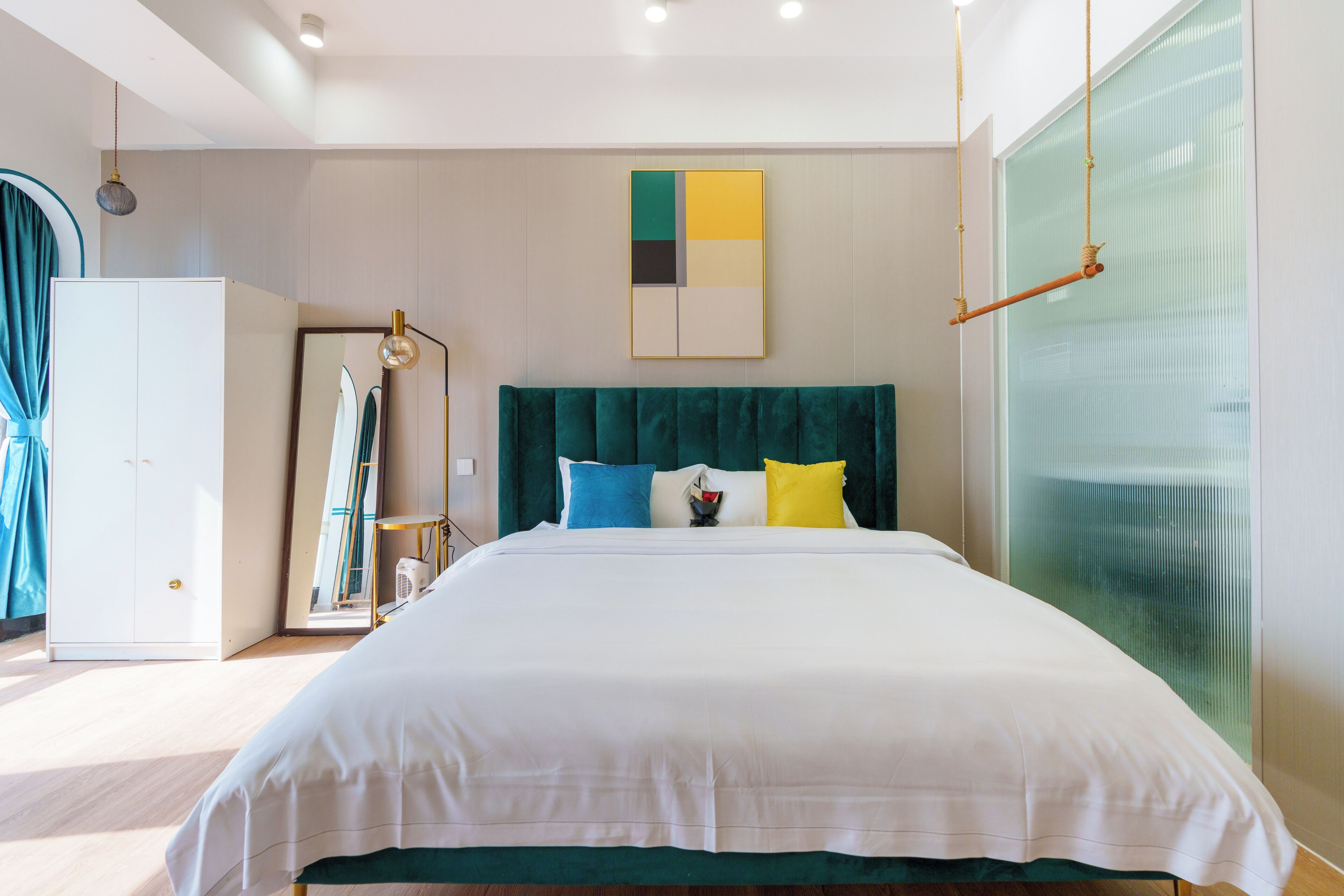 A modern hotel room with a large bed, a mirror, a wardrobe, and a window with a view.