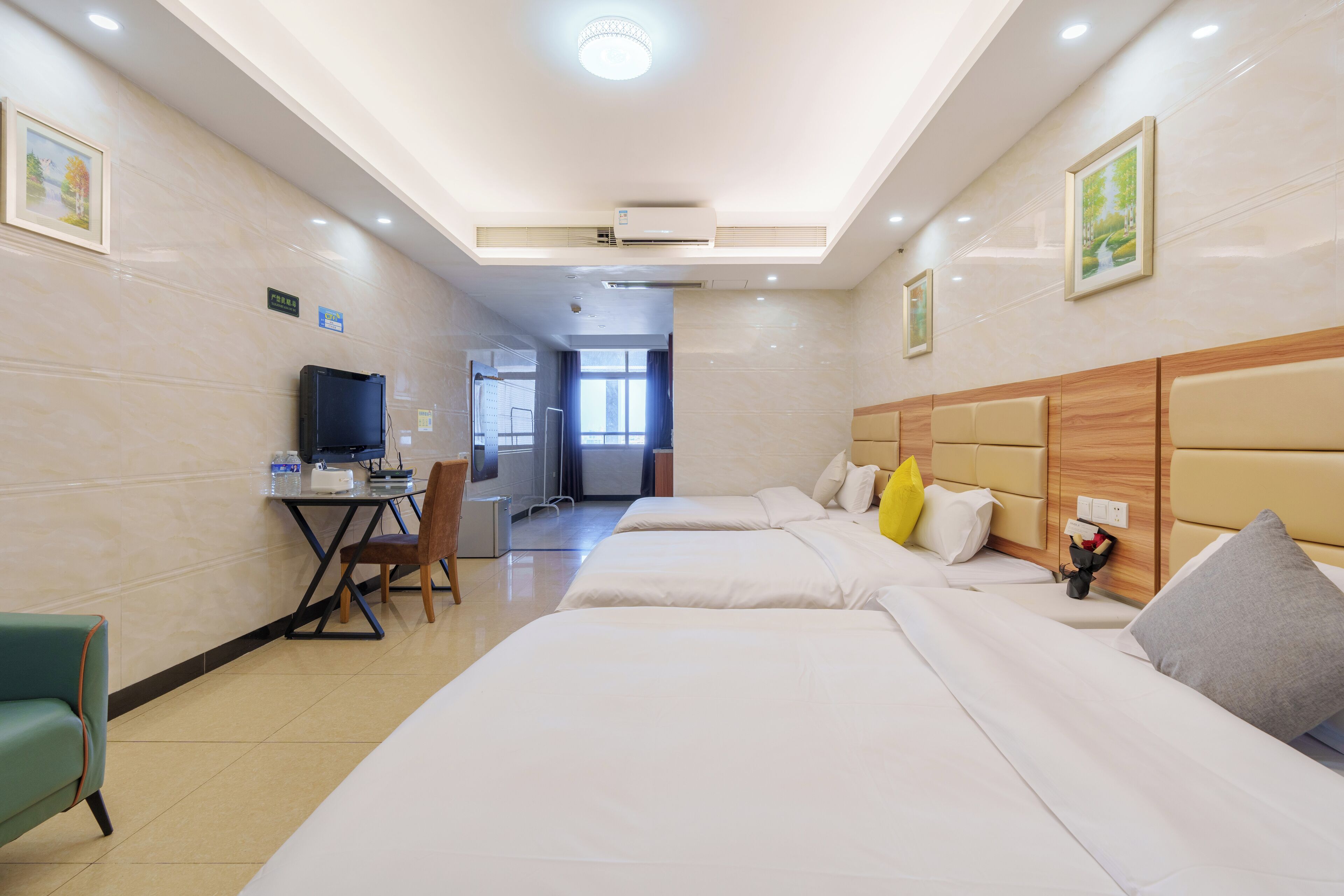 A hotel room with three beds, a desk with a computer, a chair, and a television.