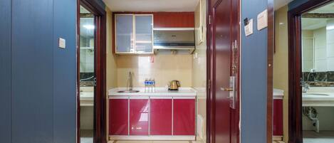 A narrow hallway with a kitchen area featuring a red and white color scheme, a stainless steel range hood, and a tiled floor.