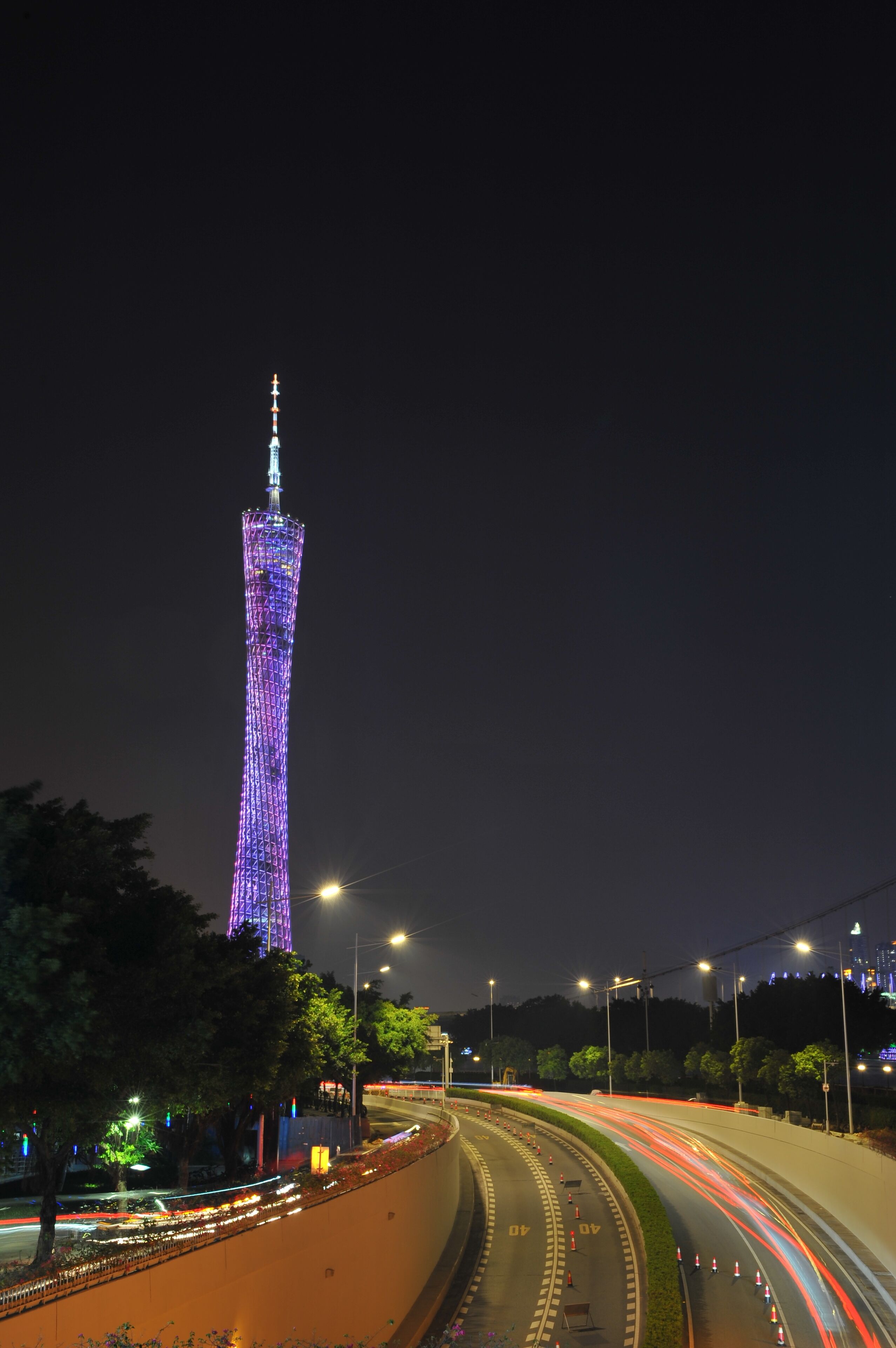 A nighttime view of a cityscape with a prominent tower illuminated in purple lights.