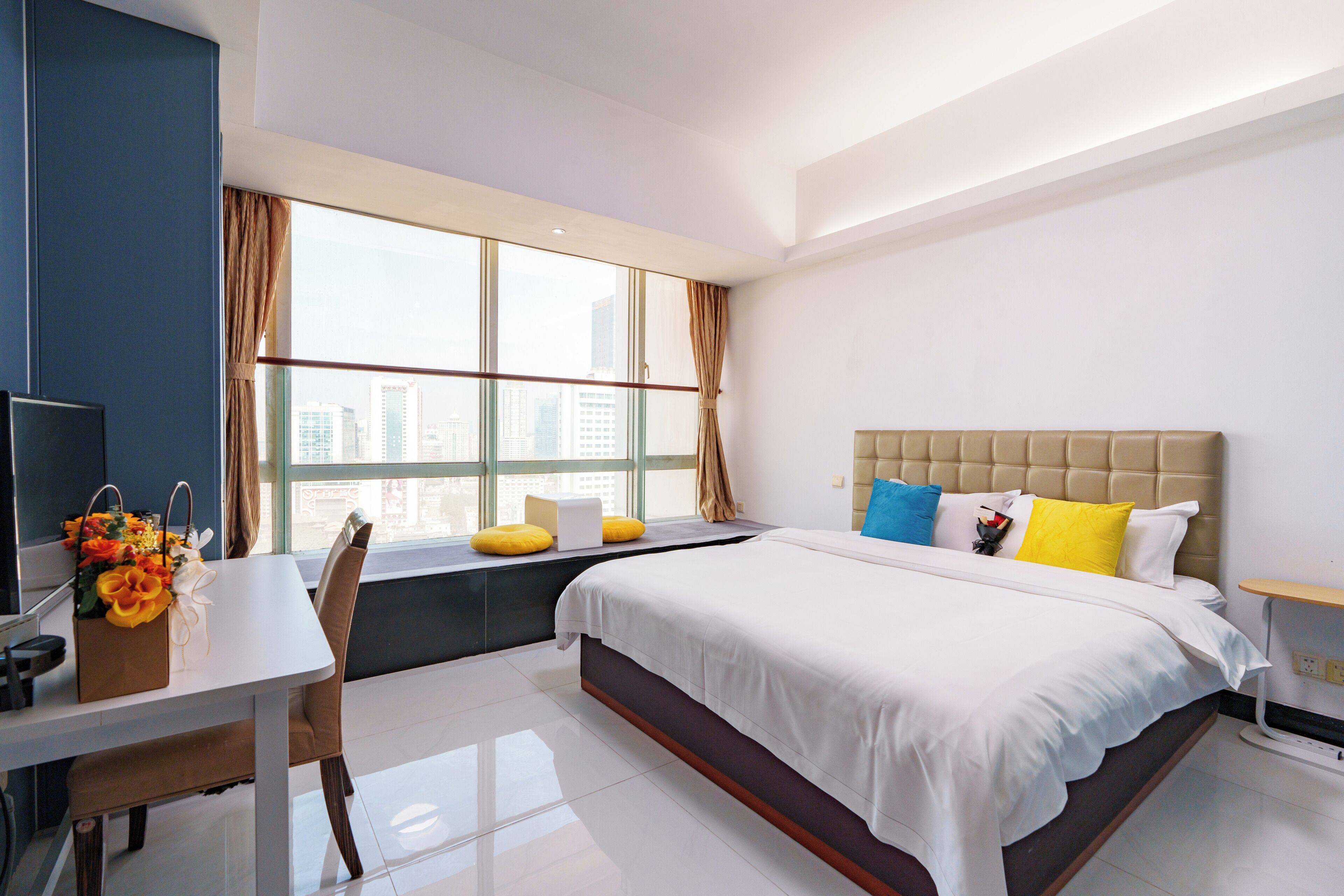 A modern hotel room with a large bed, a desk, and a window with a city view.