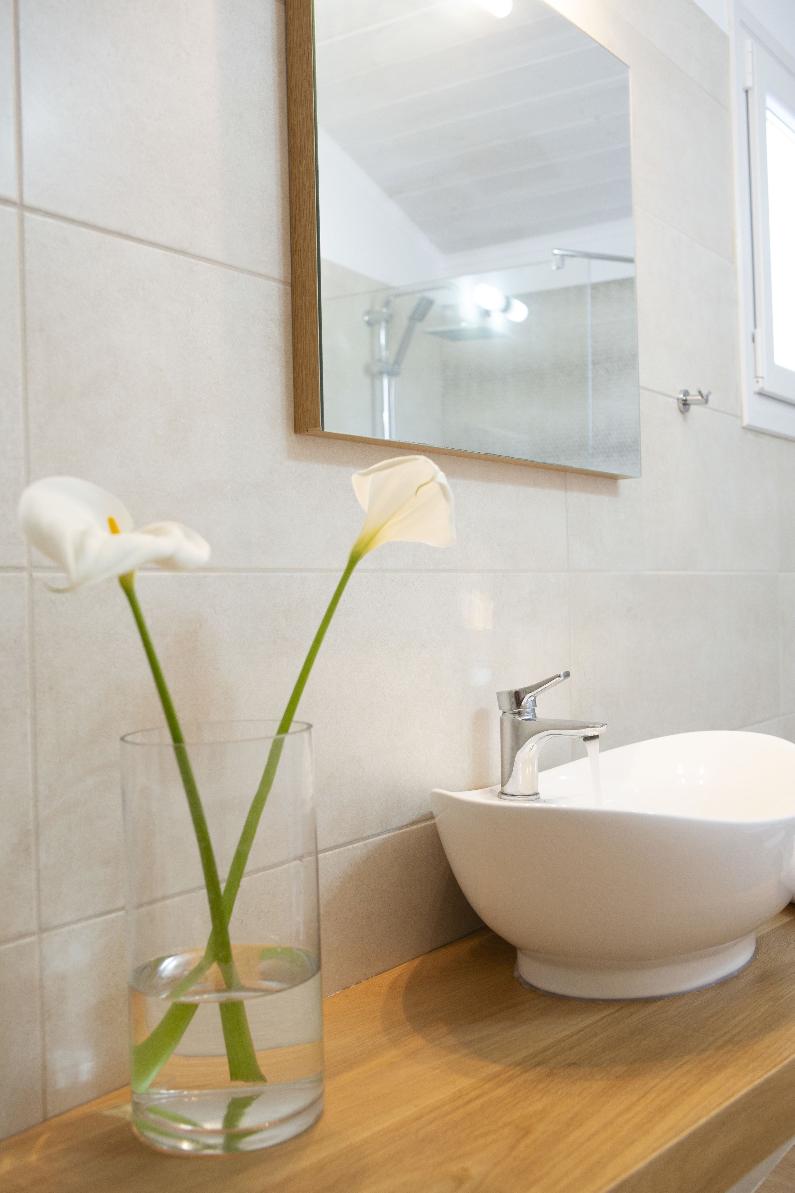 A bathroom with a white sink, a glass vase with a single white flower, and a mirror above the sink.