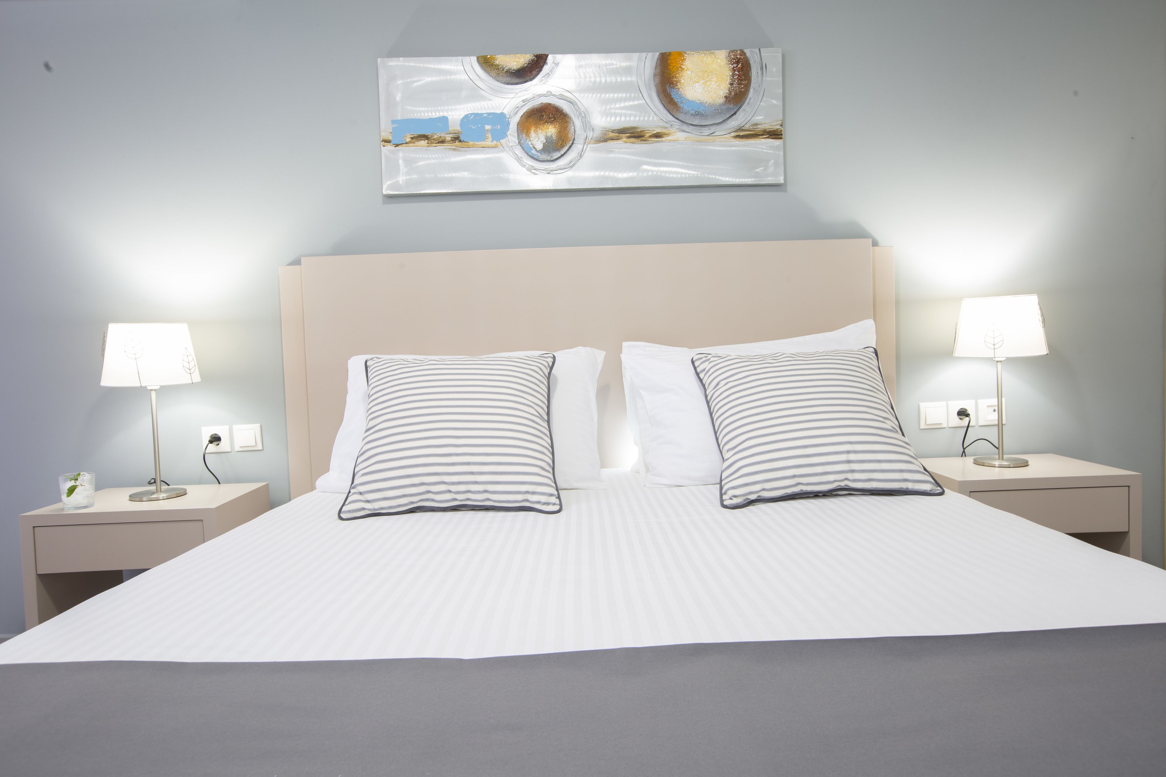 A neatly made bed with striped pillows, two bedside tables with lamps, and a wall-mounted abstract painting.