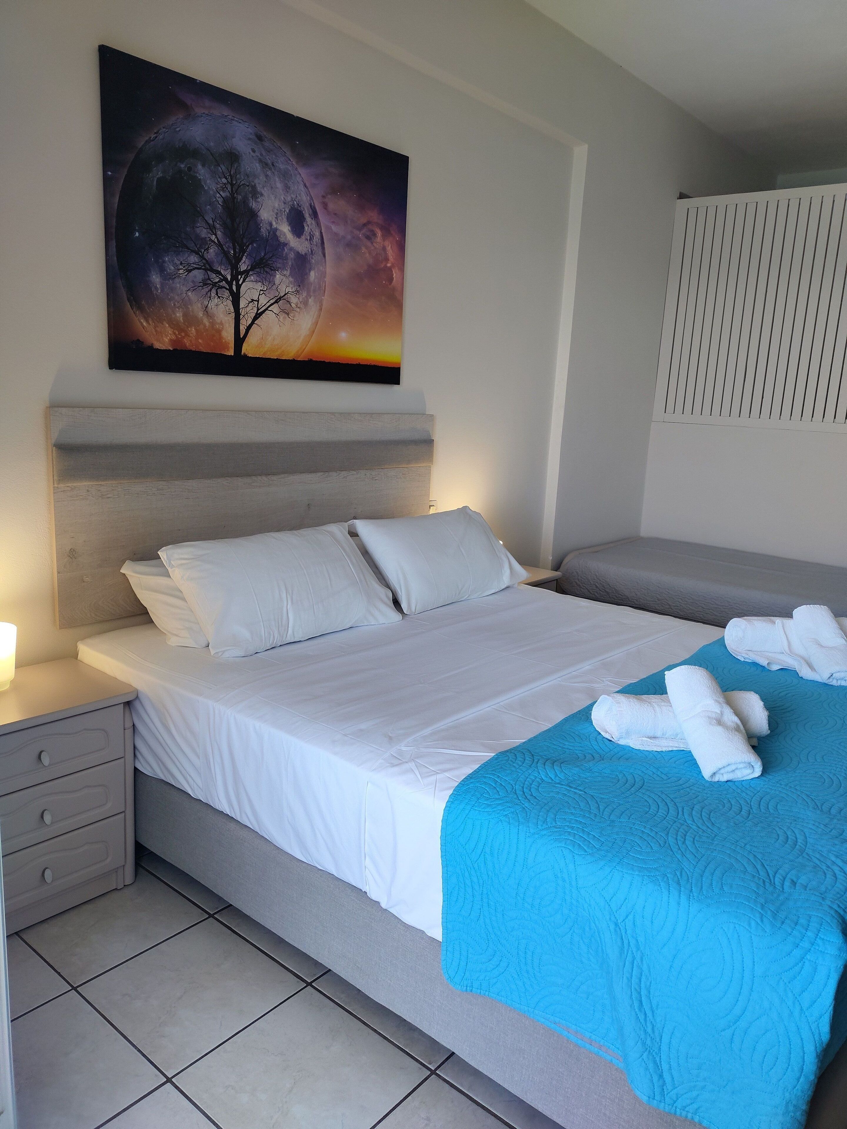 A neatly made bed with white linens, a blue quilt, and rolled towels on a blue bedspread.