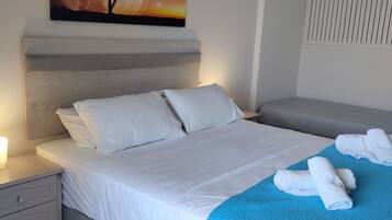 A neatly made bed with white linens, a blue quilt, and rolled towels on a blue bedspread.