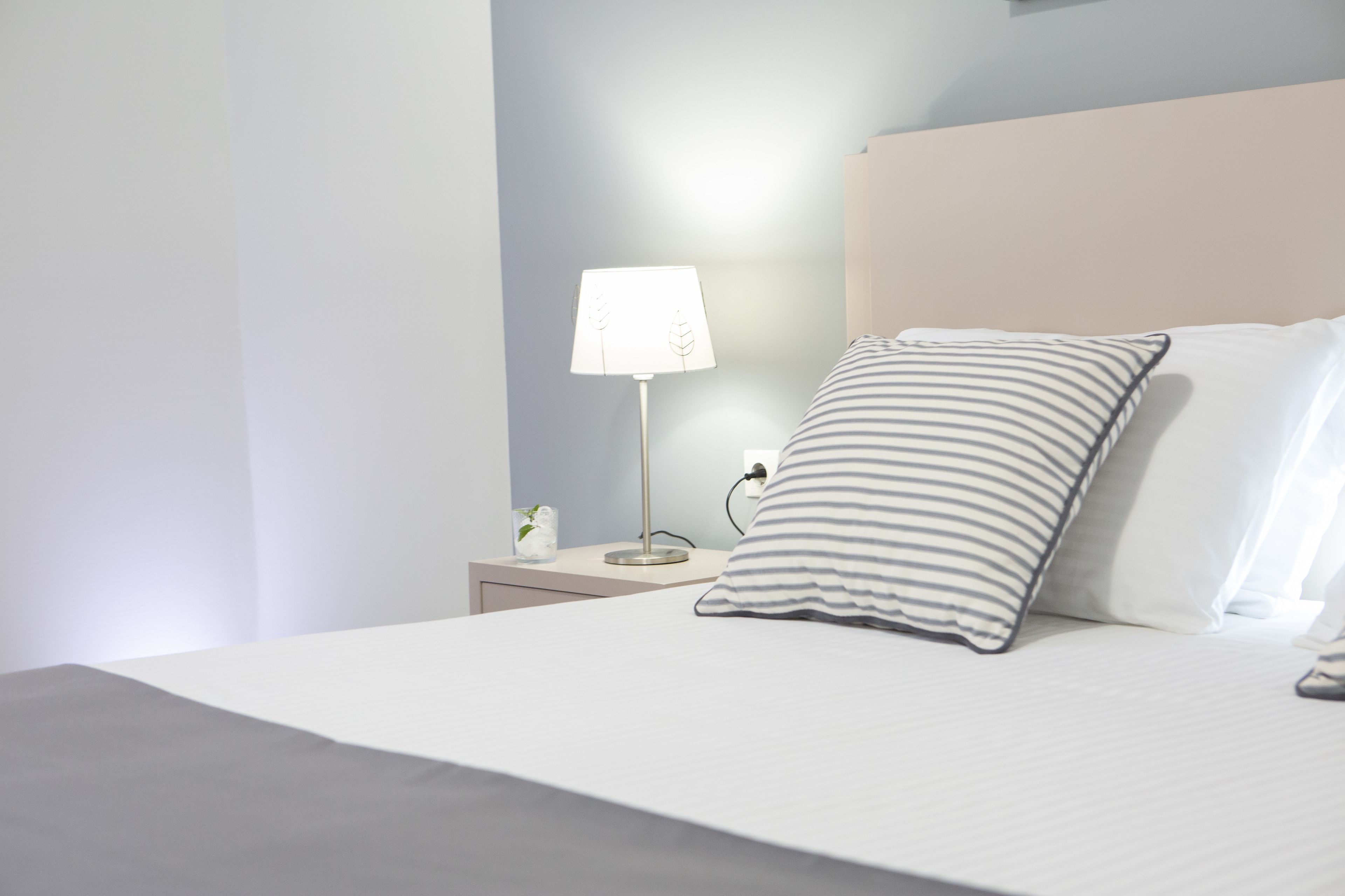 A neatly made bed with a striped pillow and a bedside lamp on a nightstand.