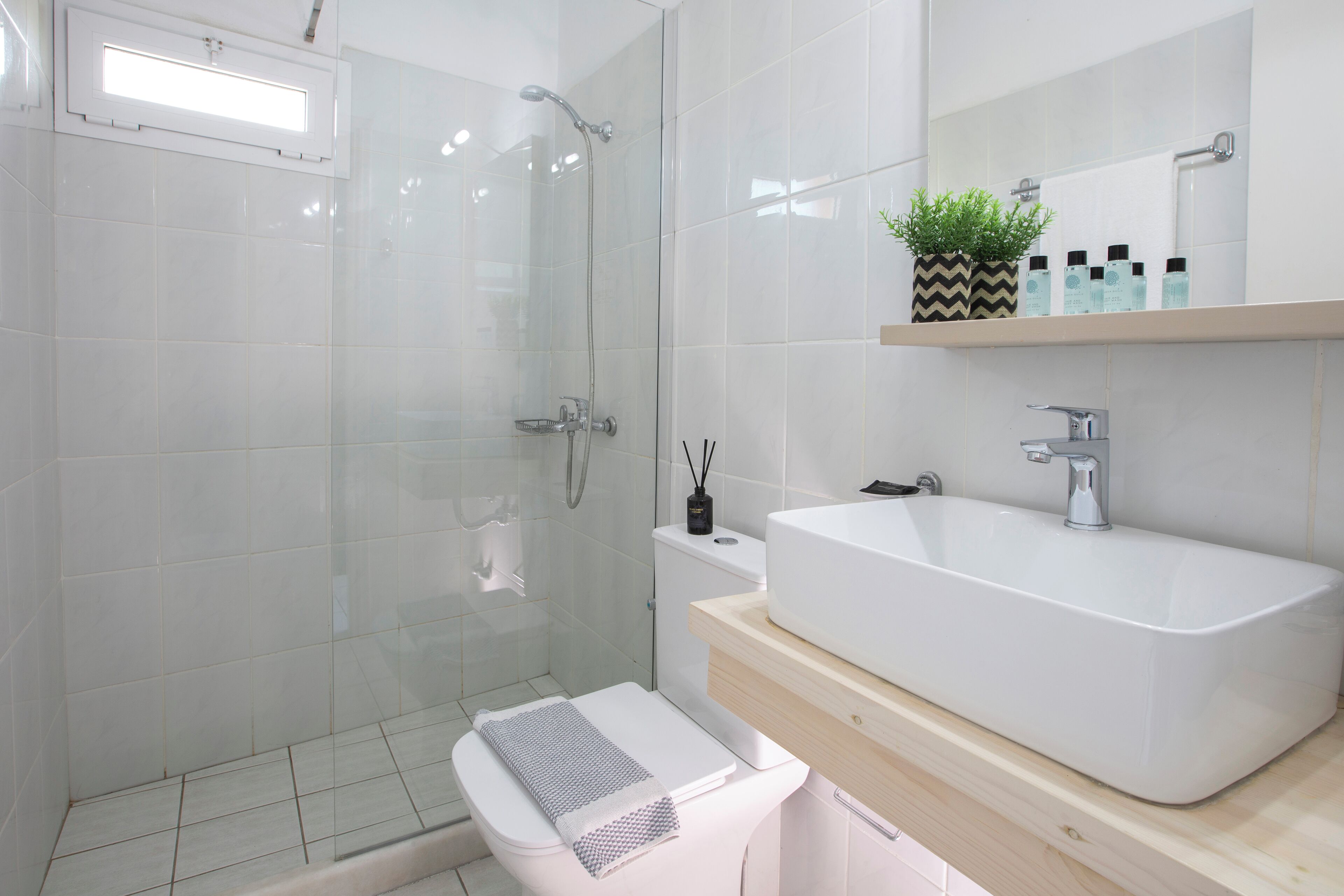 A modern bathroom with a glass-enclosed shower, a white sink, and a small shelf with toiletries.