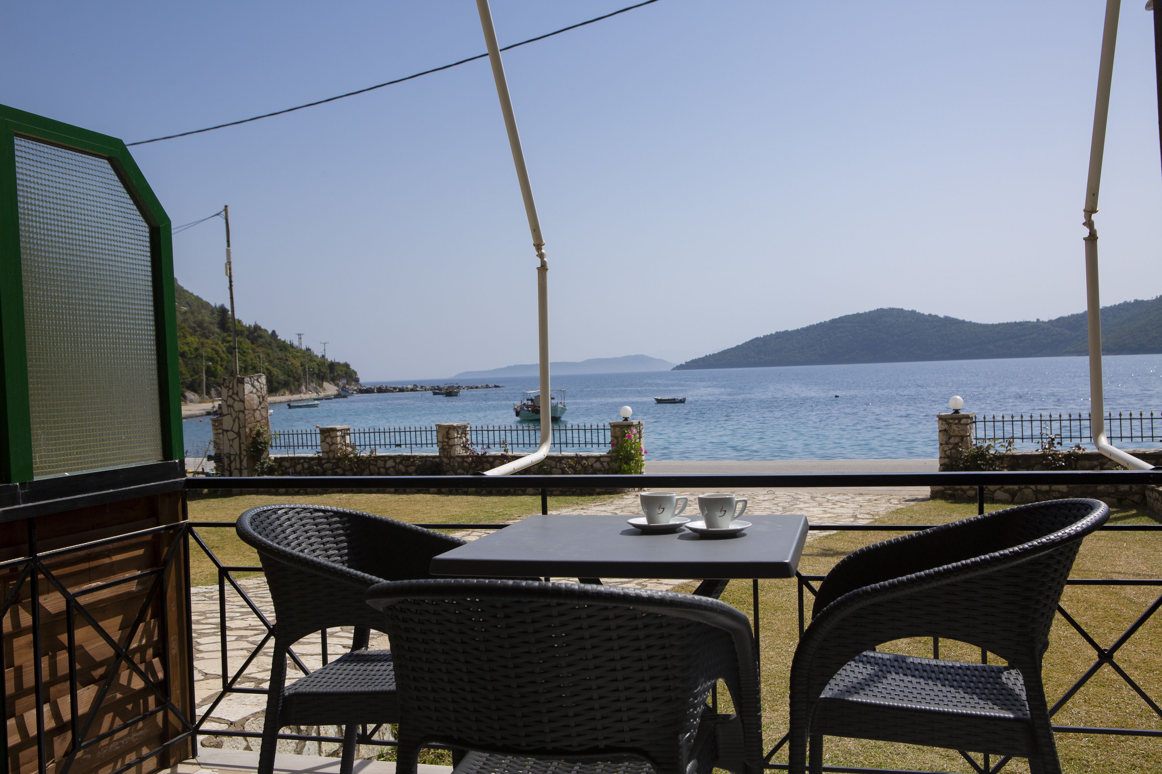 A terrace with two wicker chairs and a table, overlooking a body of water with boats and a distant mountain.