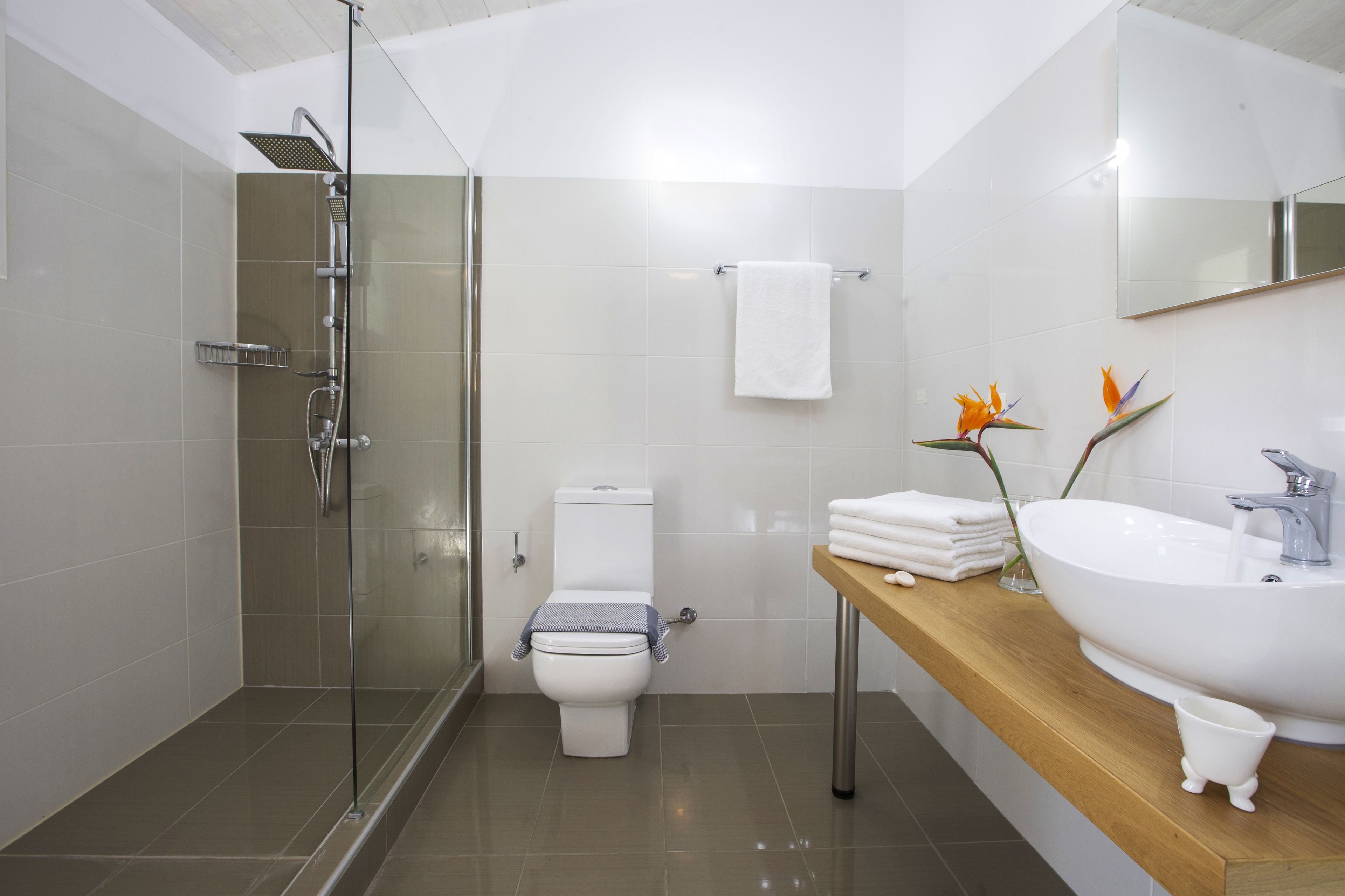 A modern bathroom with a glass-enclosed shower, a toilet, and a wooden vanity with a sink and mirror.