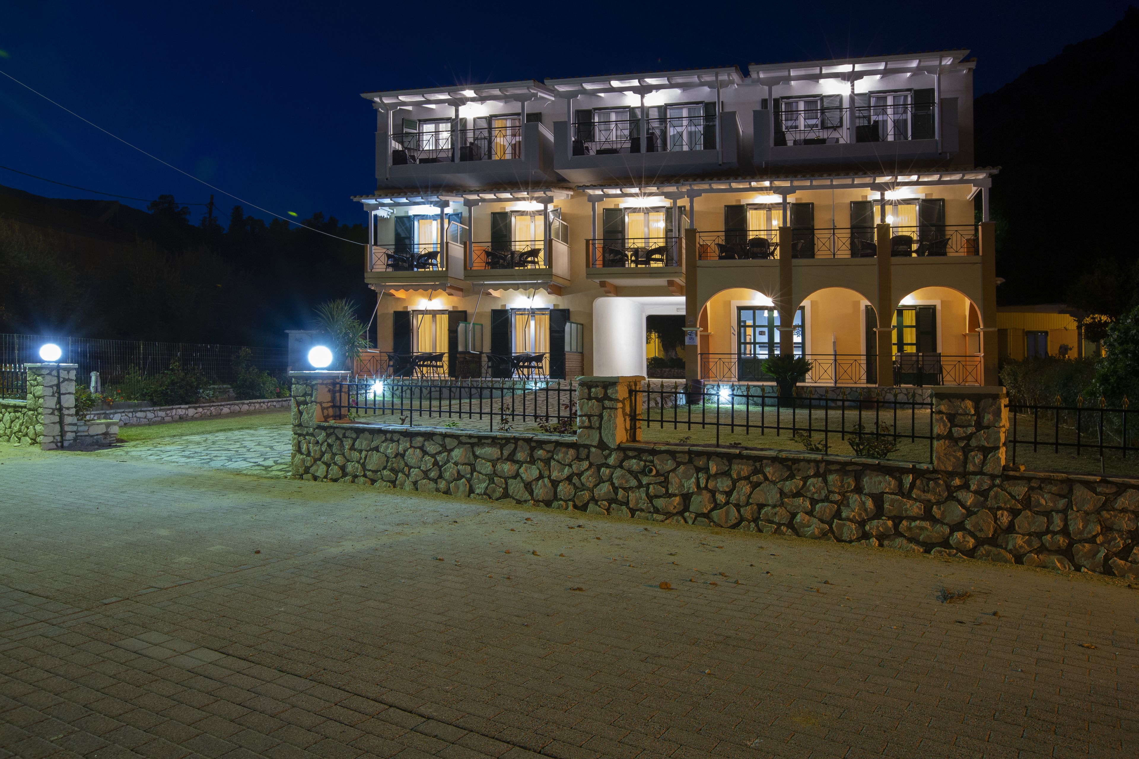 A multi-story building with balconies and a stone wall in front.